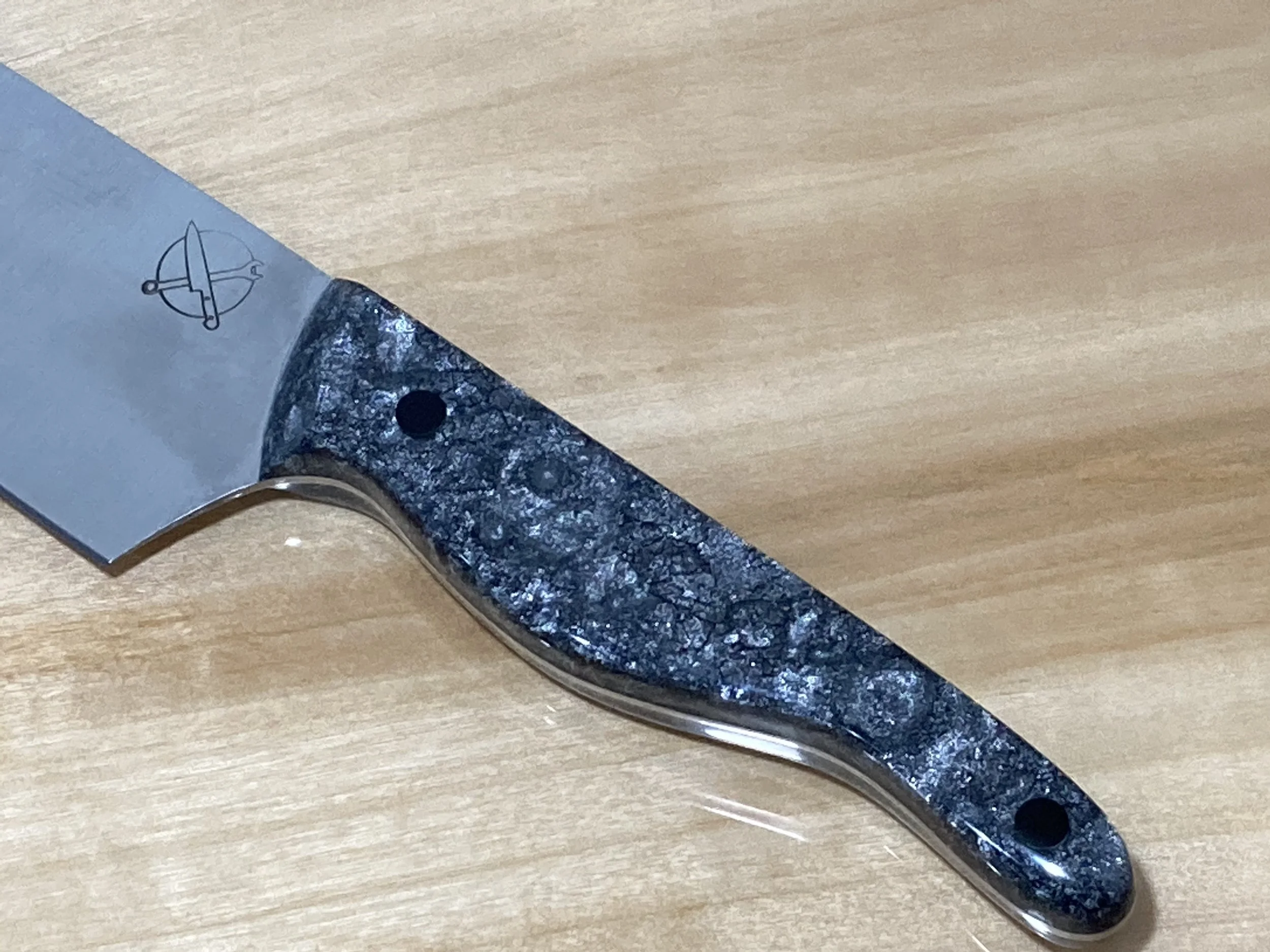 Close-up of a kitchen knife with a black and gray patterned handle on a wooden surface.