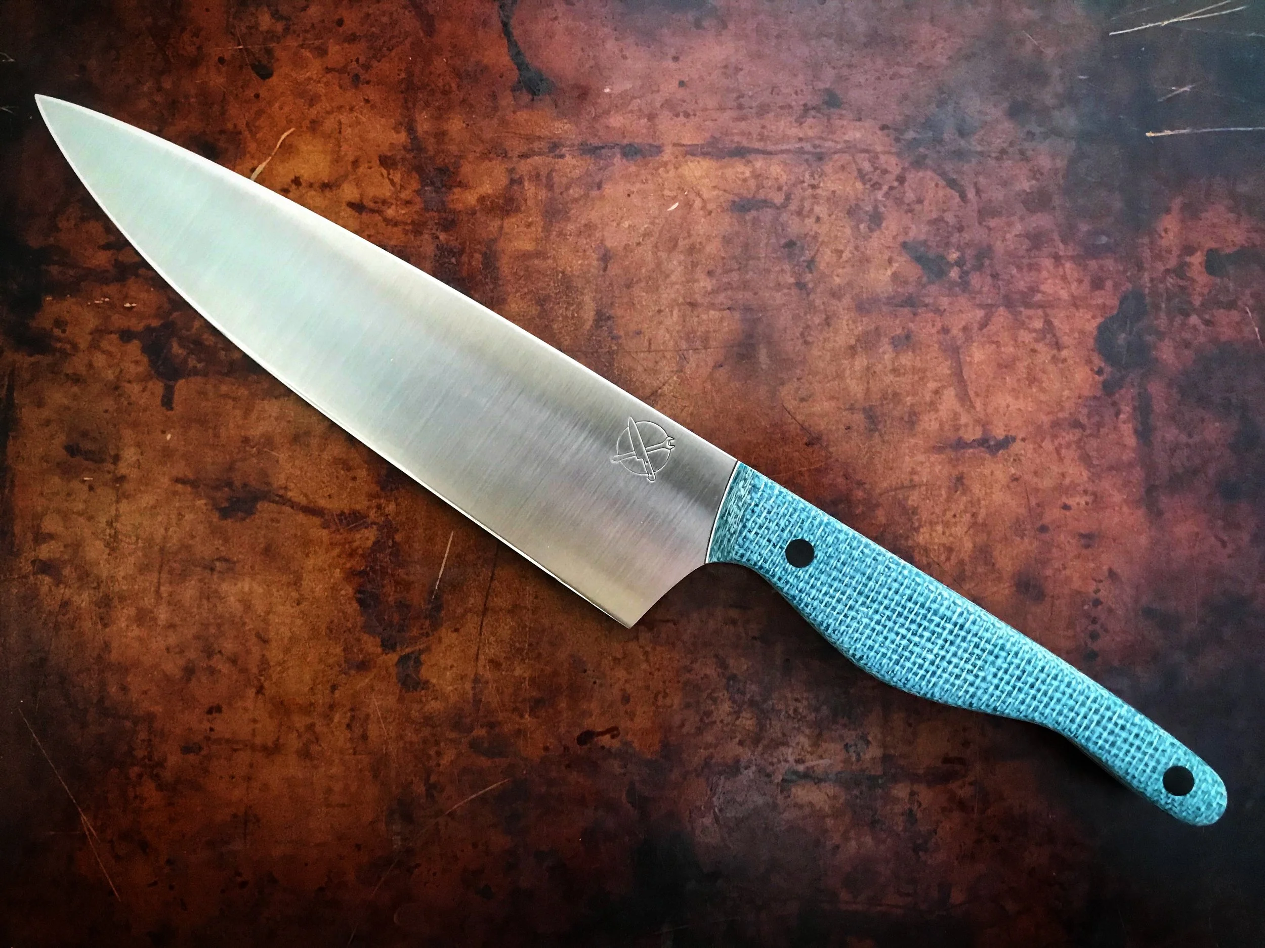 A stainless steel chef's knife with a blue textured handle, resting on a wooden surface.