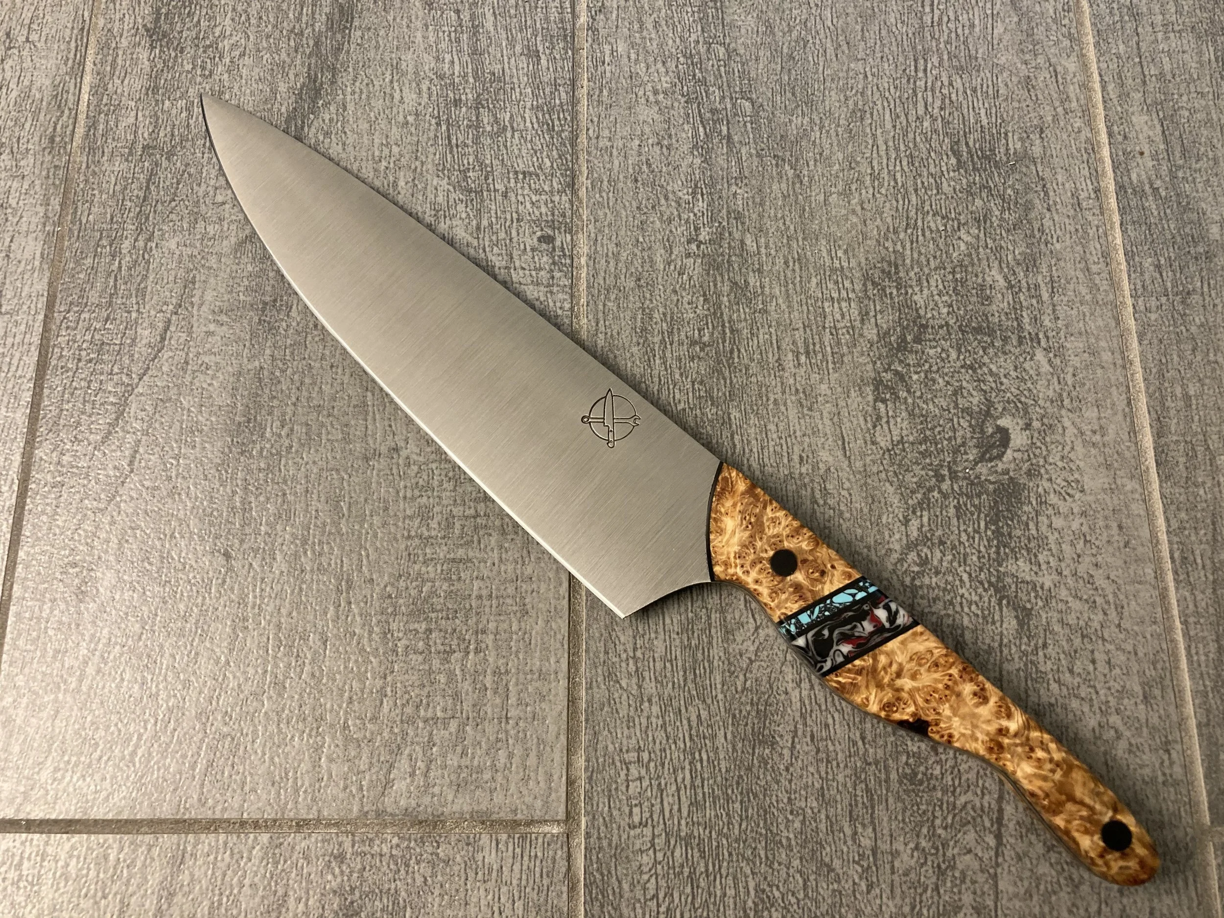 The Mule — 8" Chef's Knife in AEB-L | Montana Cedar Burl, Teal Stone Segment & NYC Street Art Resin | Solid Carbon Fiber Pins — SOLD | By far the most ambitious handle brief ever brought to this shop. Three cultural identities. One knife. Montana ced