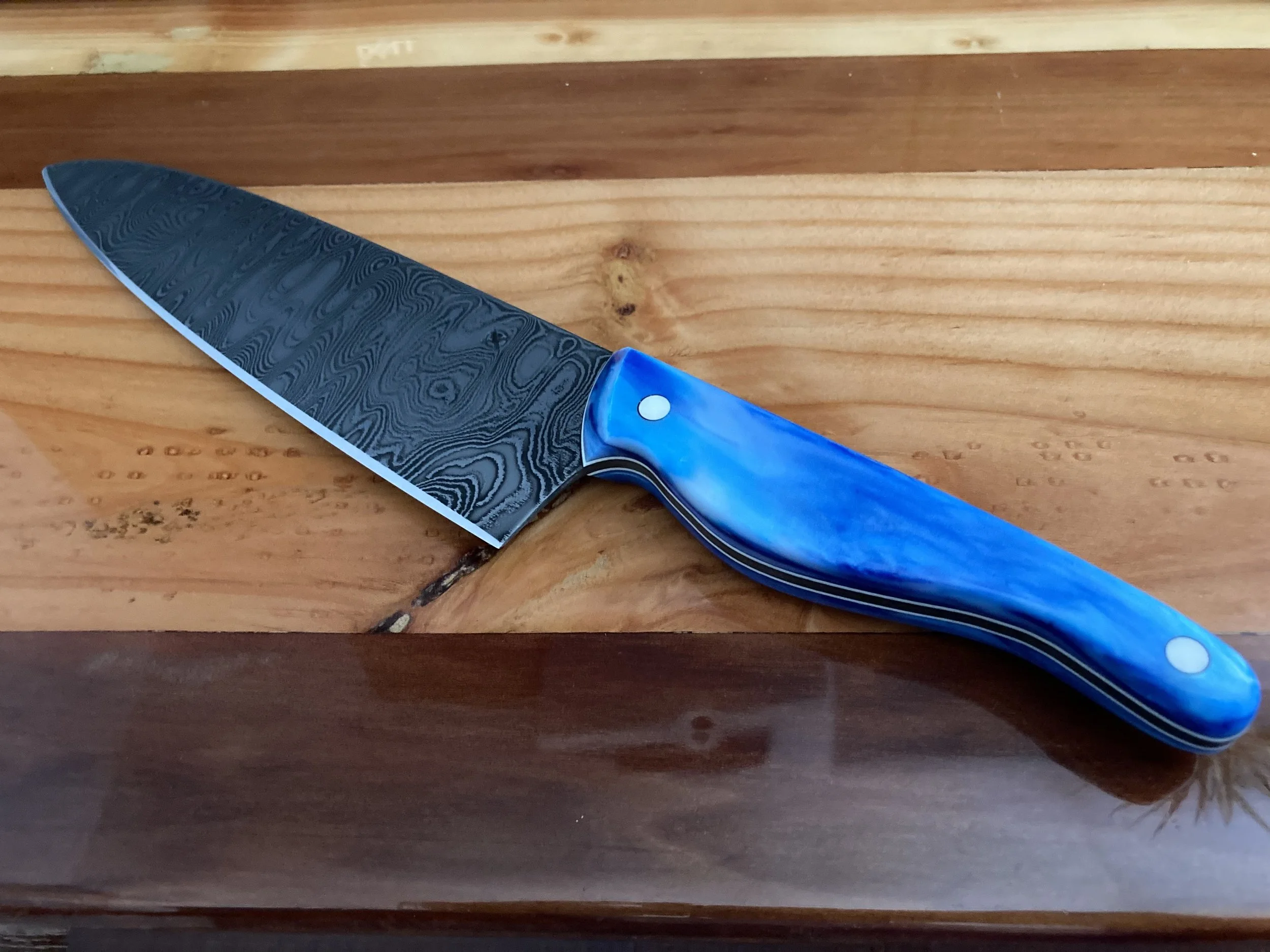 A chef's knife with a Damascus steel blade and a blue marbled handle resting on a wooden surface.