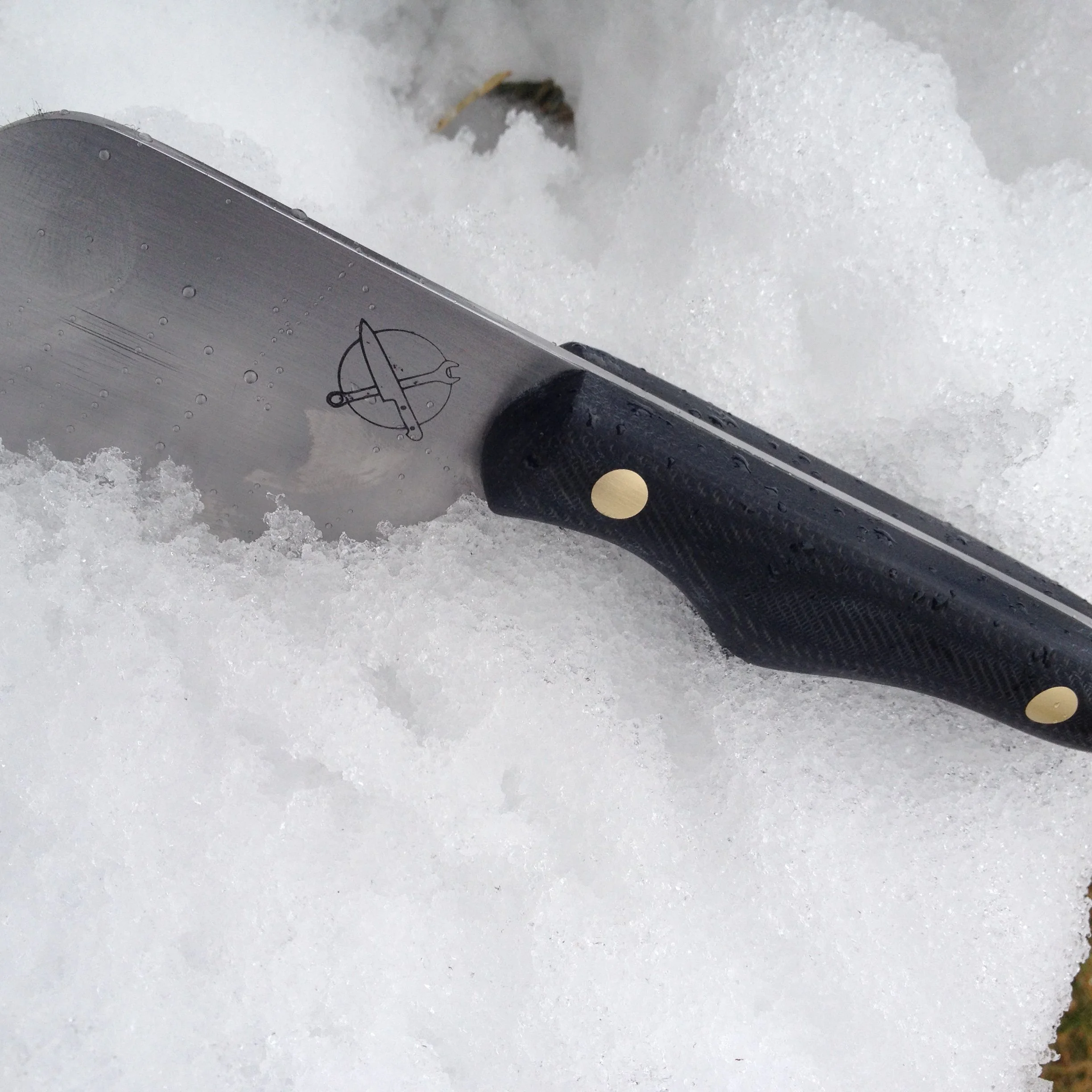 Blue Collar Blades 'prison shank' mini-cleaver knife with reposed denim scales and solid brass pins resting in a mound of fresh snow.