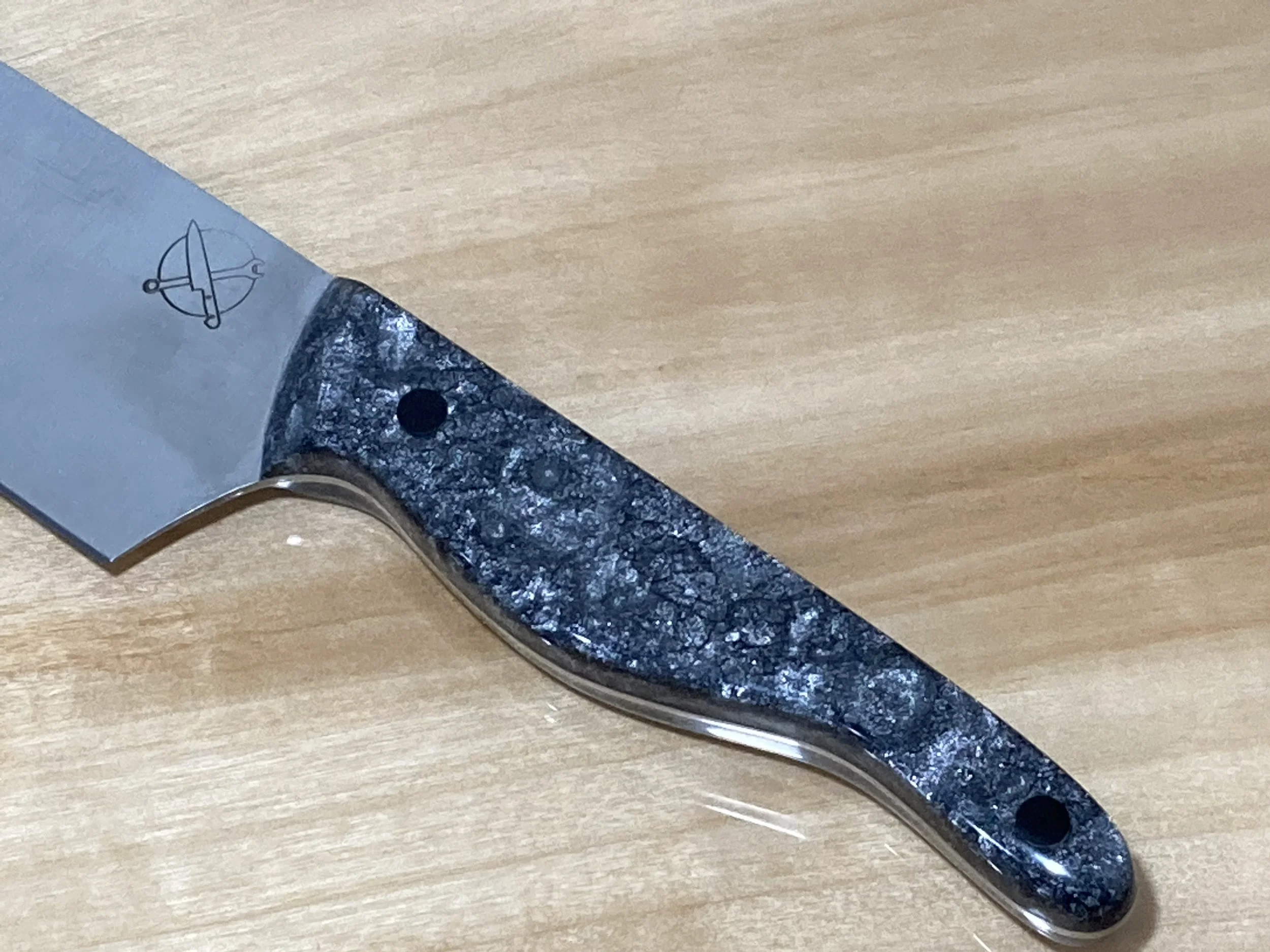 Close-up of a knife with a metal blade and a dark, textured handle resting on a wooden surface.