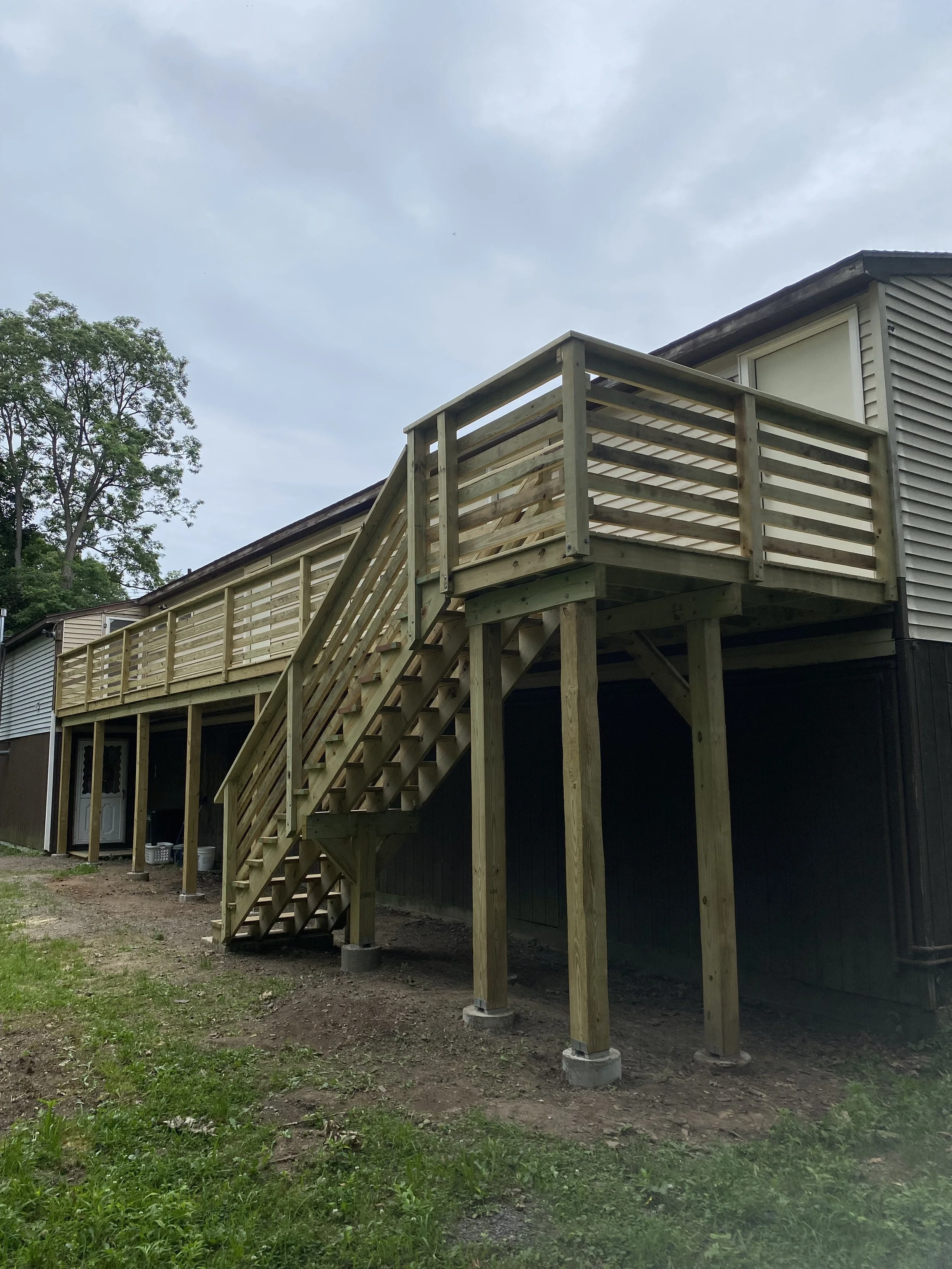 Wooden deck and staircase attached to the back of a house, with support posts and a privacy railing.