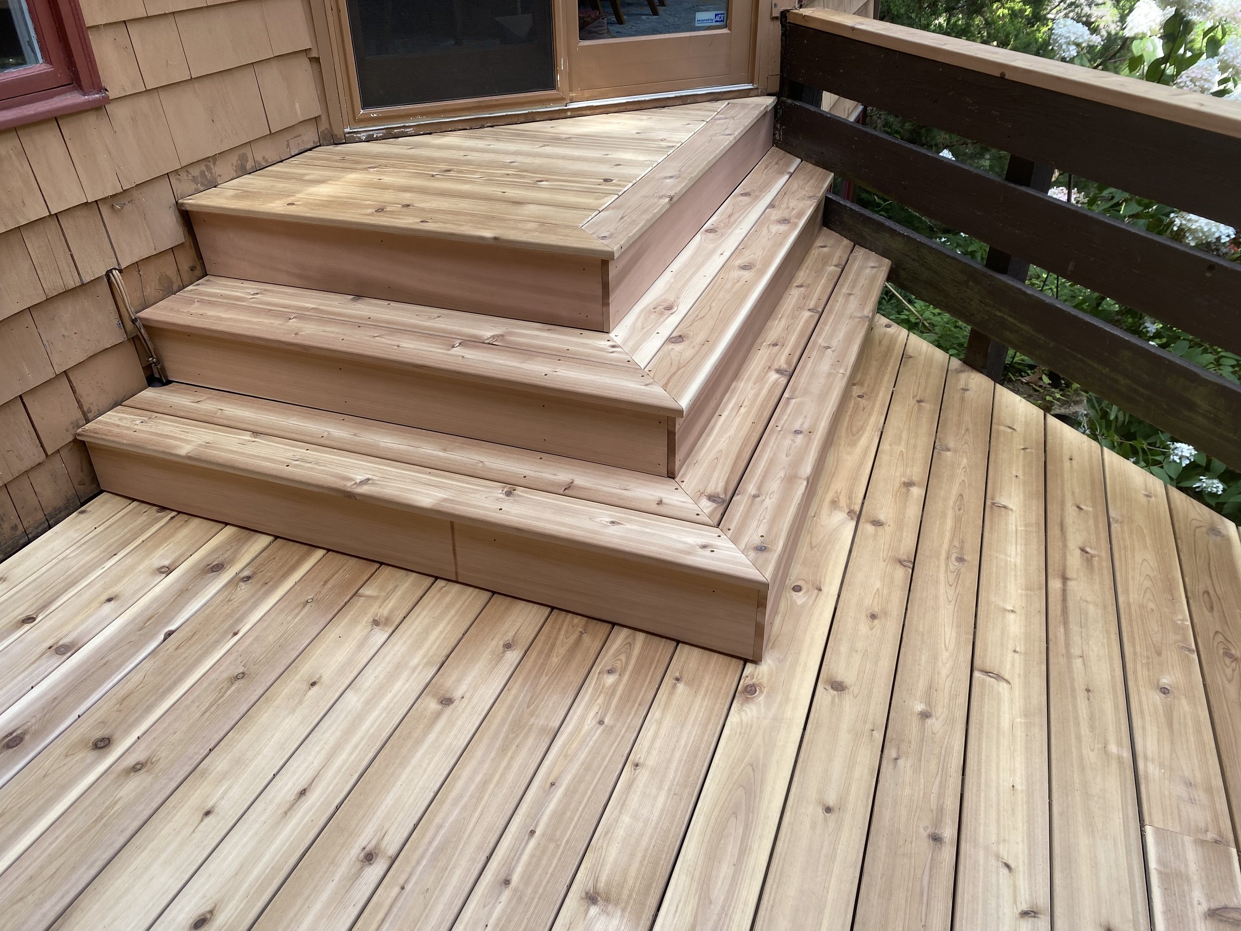 Newly built wooden deck with stairs and railing, attached to a house with a glass door.
