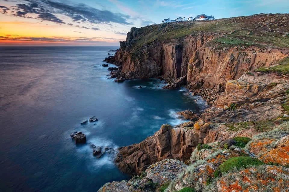 Cliffs overlooking the ocean at sunset with houses on top of the cliffs and rocks along the shoreline.