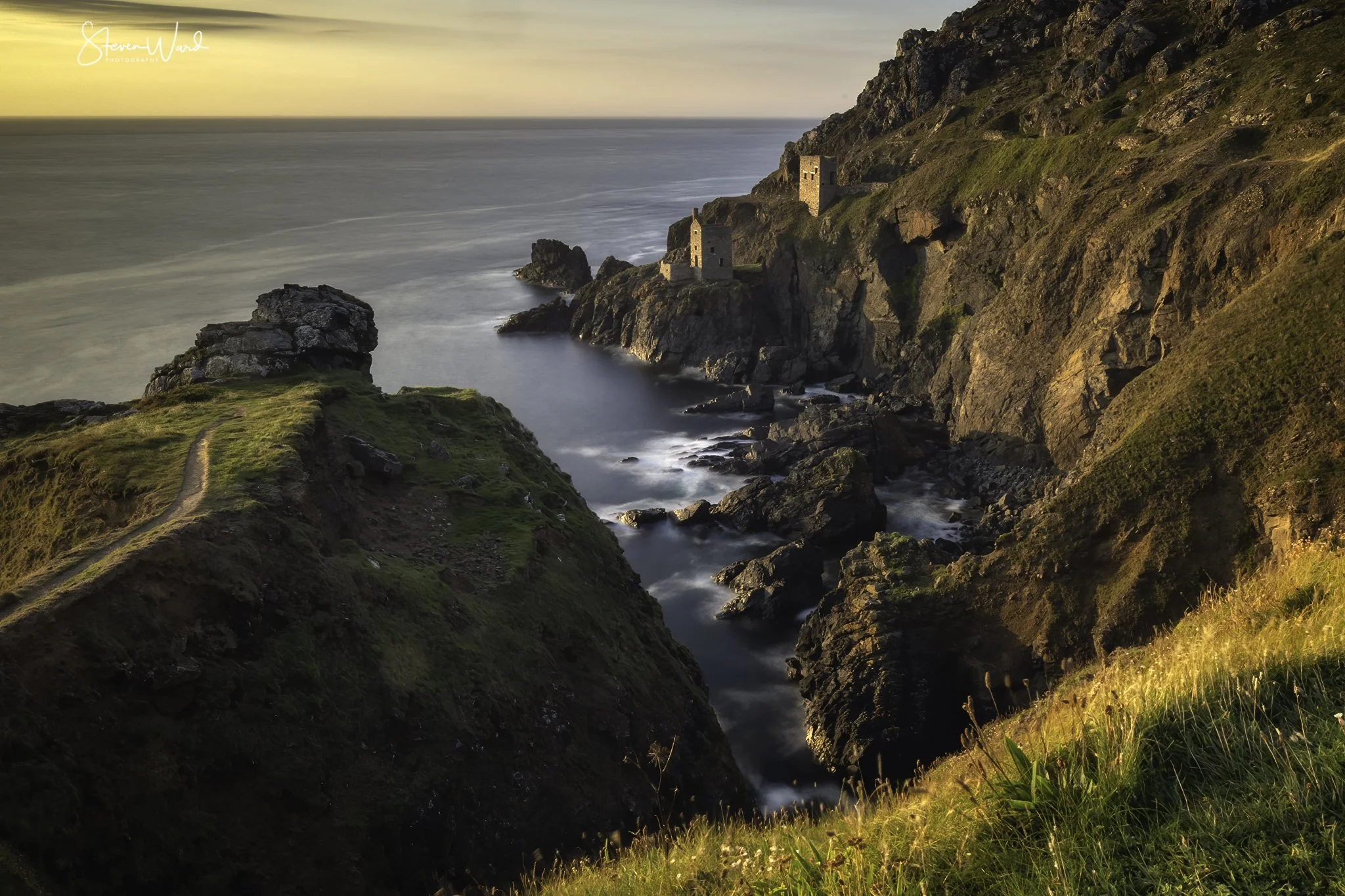 Cliffside with green grassy paths and ruins overlooking the ocean at sunset
