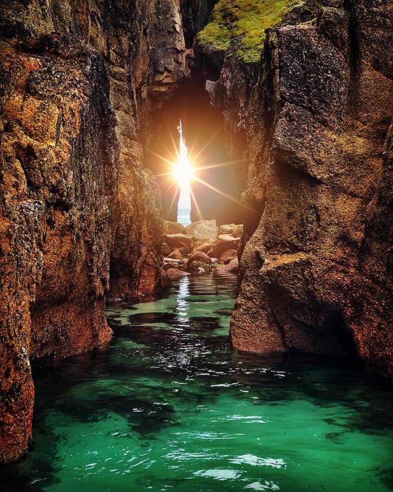 Sunshine shining through a narrow rocky canyon with green water below.