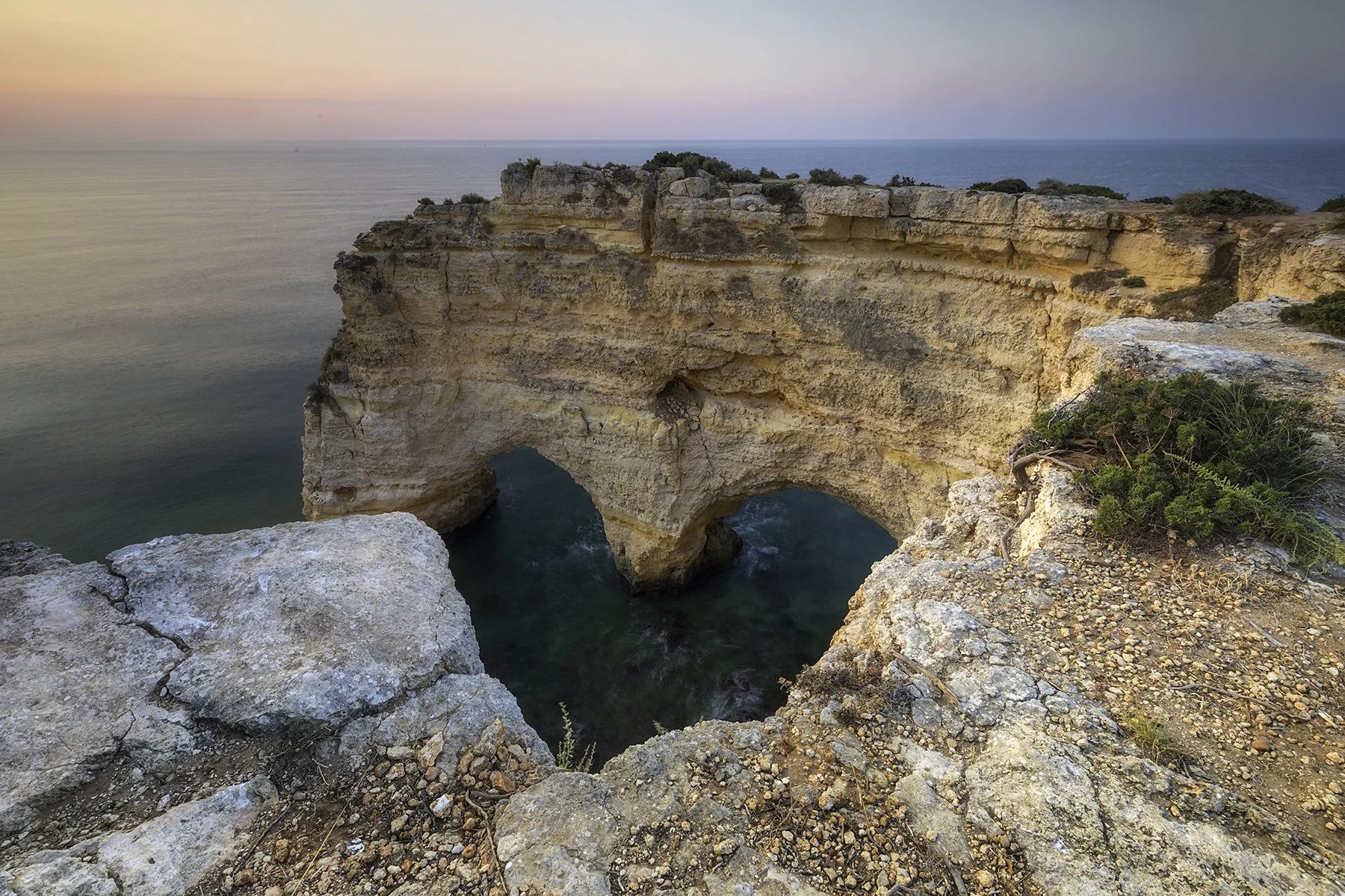 Cliffside with natural arches overlooking the ocean during sunset