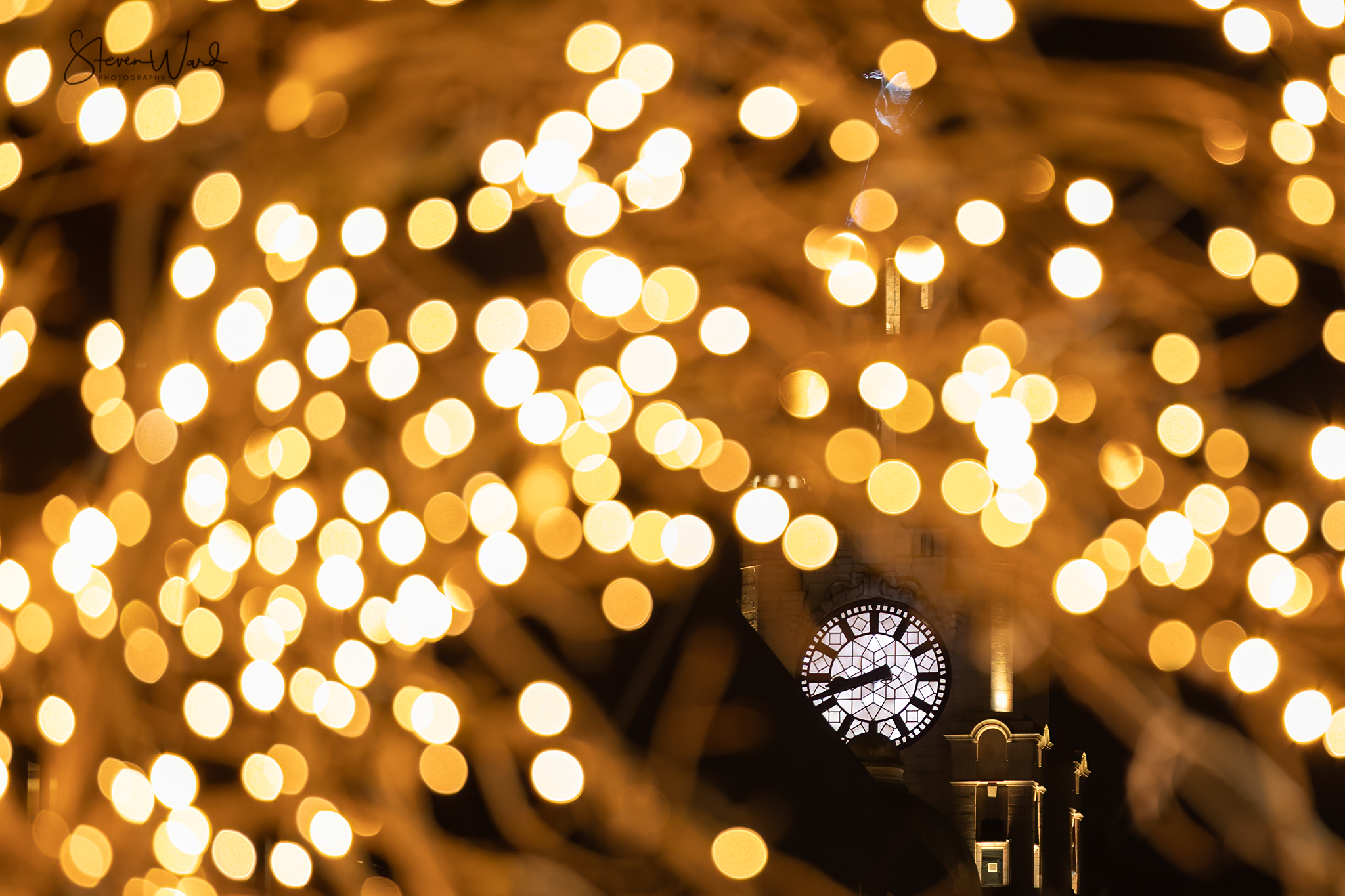 Clock tower illuminated at night with large, bright bokeh lights in the foreground.