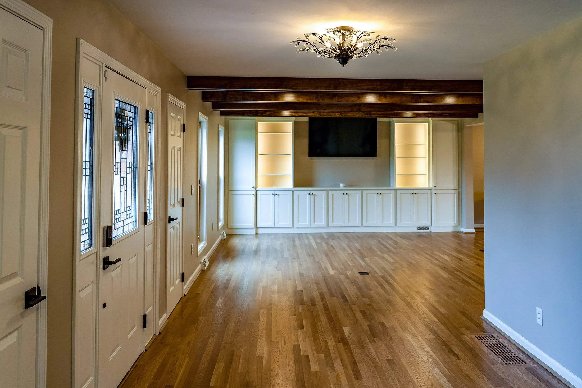 Complete First Floor Remodel by KBC Inc. Side view of open concept entry. Plank wooden flooring. LED can lighting. Ornate floral lighting fixture in center. External entry door on left side of photo. Lighted shelving, storage cabinets, and TV alcove 