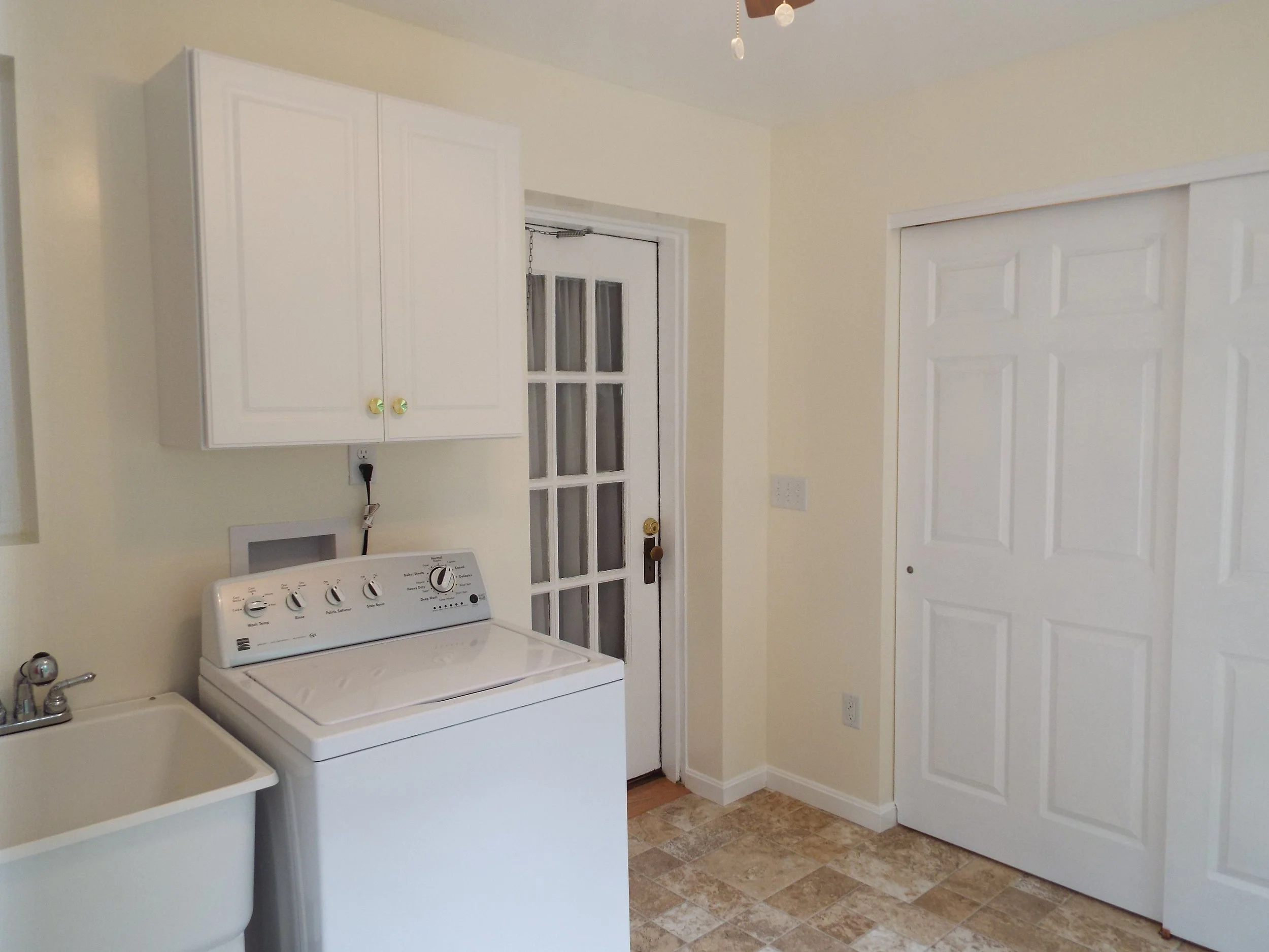 Inside view of completed laundry room, with washer, laundry sink, tile floor and storage cabinets