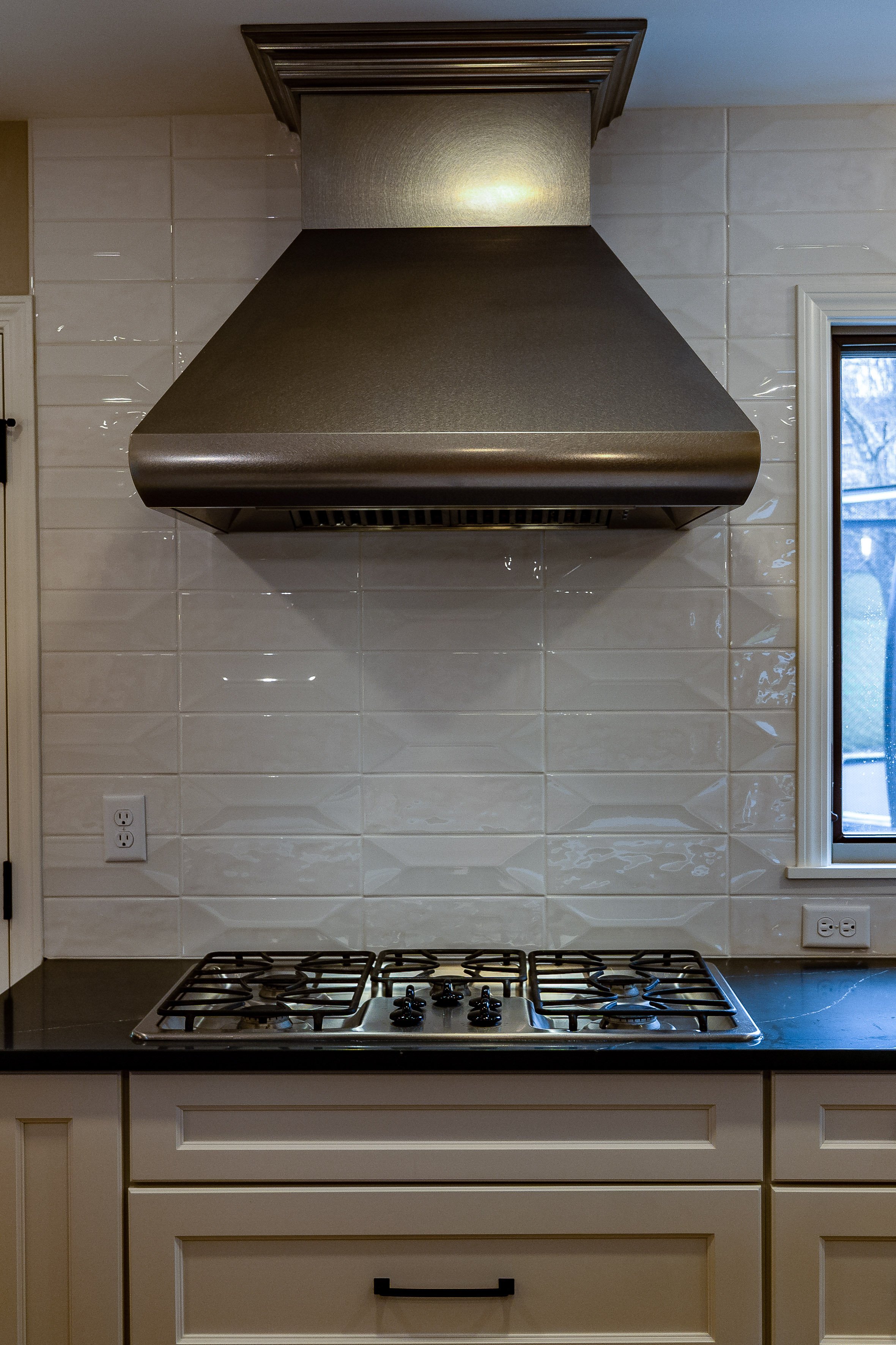 Complete First Floor Remodel by KBC Inc. Closeup view of exhaust hood over gas stove burners mounted in dark countertop. White subway tile backsplash. 