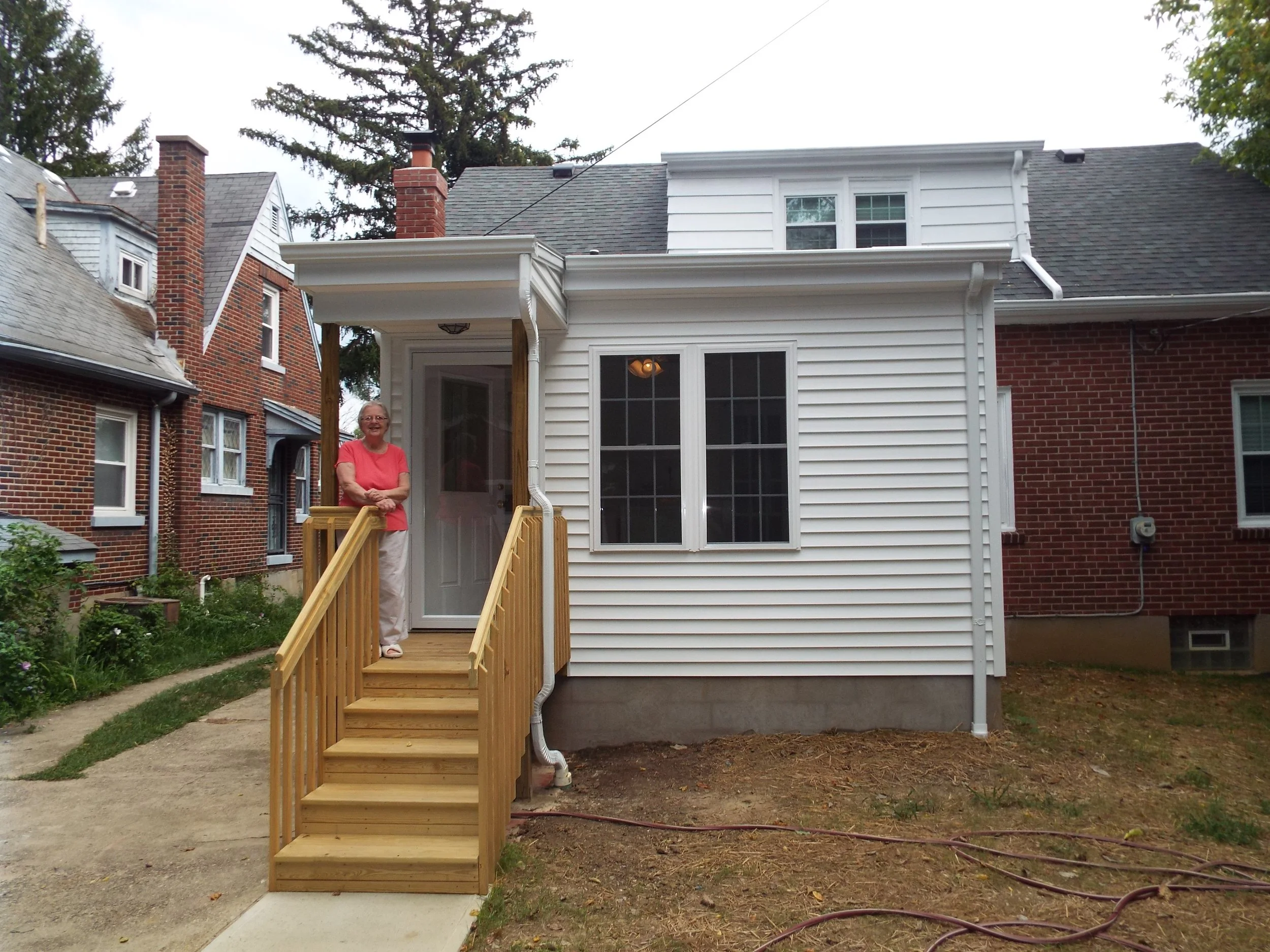 Outside view of completed project - Woman smiling, standing on porch steps 