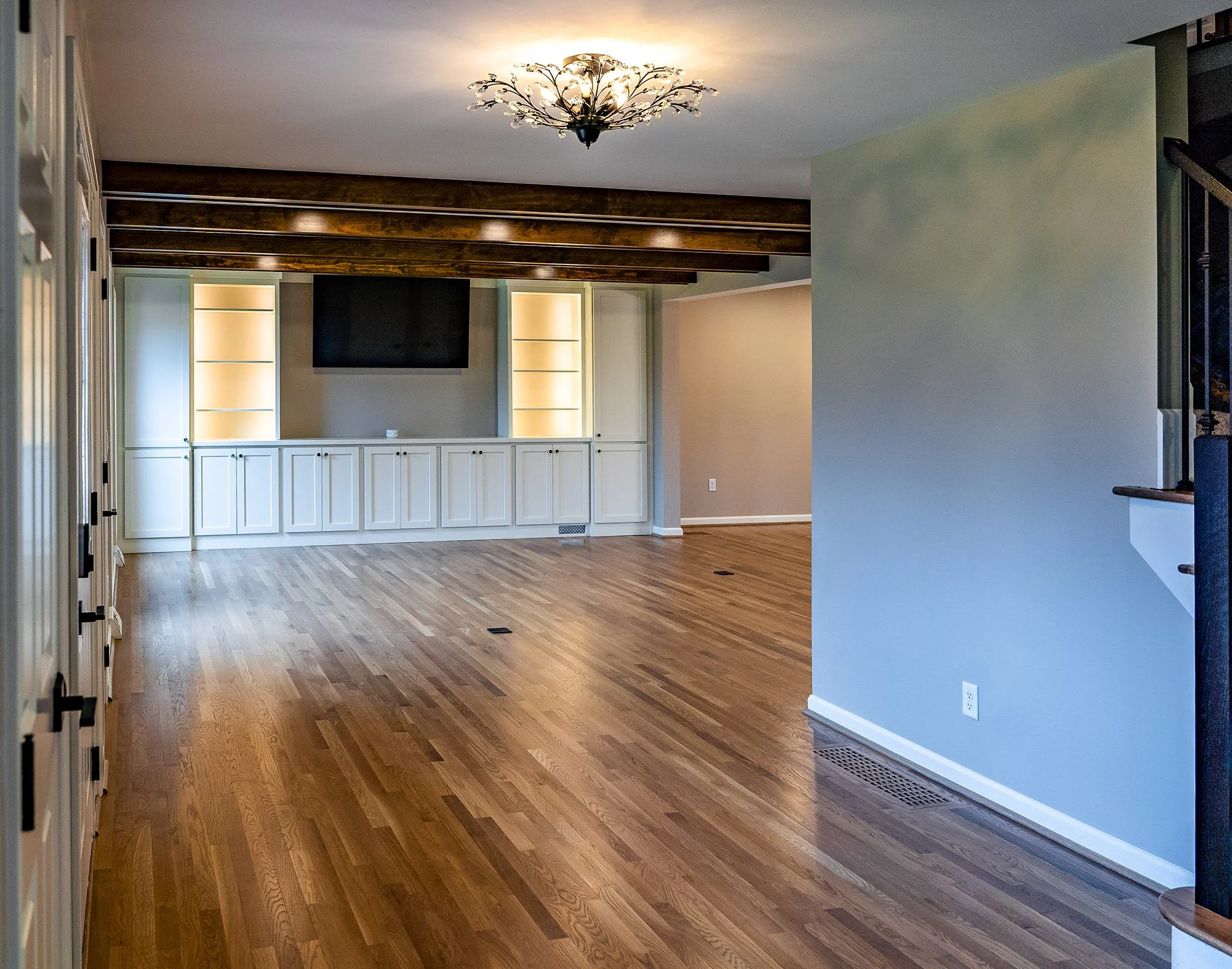 Complete First Floor Remodel by KBC Inc. Side view of open concept entry. Plank wooden flooring. LED can lighting. Ornate floral lighting fixture in center. External entry door on left side of photo. Lighted shelving, storage cabinets, and TV alcove 