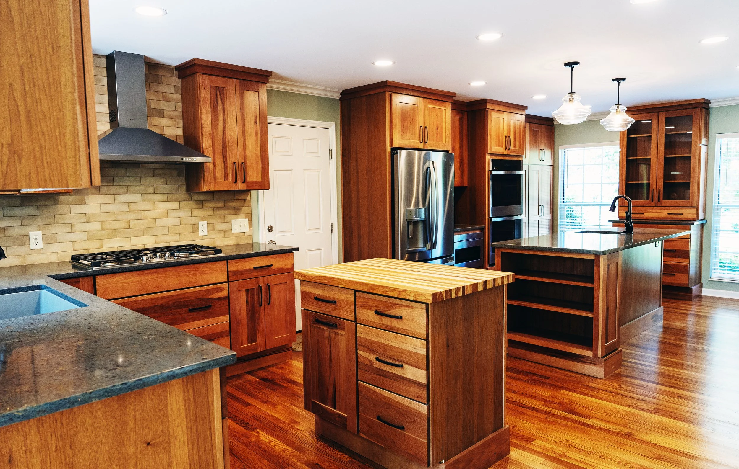 KBC Construction - Whole House Remodel in Lakeside Park, KY. Remodelled kitchen. Photo shows close faucet and countertop,  stovetop with stainless steel range hood, small butcher block island, large island with sink, stainless steel refridgerator, di