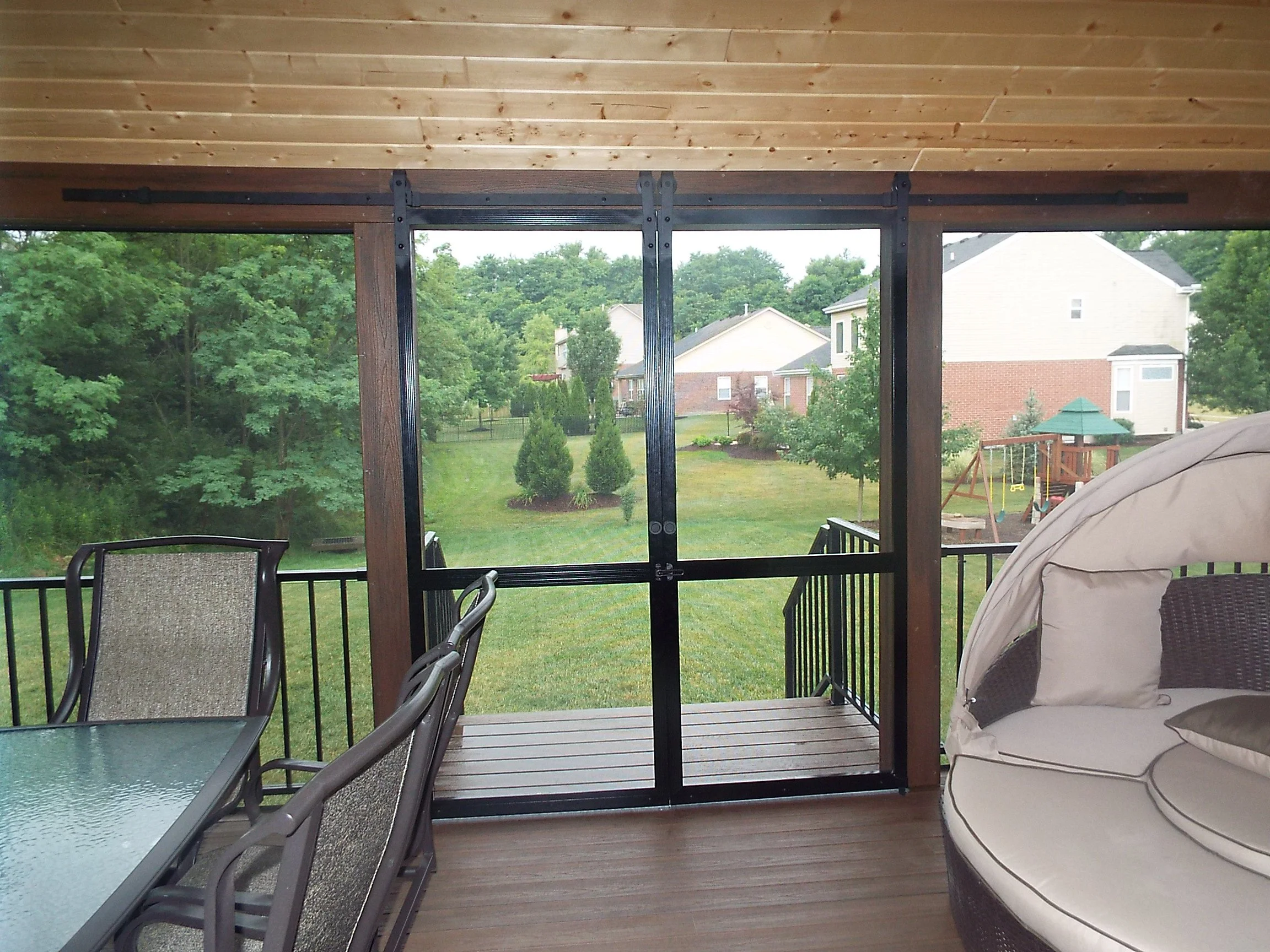 Screened in porch. Wooden bead board ceiling. Wooden floor. Round chaise lounge on right of photo. Outdoor patio table and  chairs on left of photo. Screened doors lead to stairs into yard. Large screened windows with metal railing look out into yard