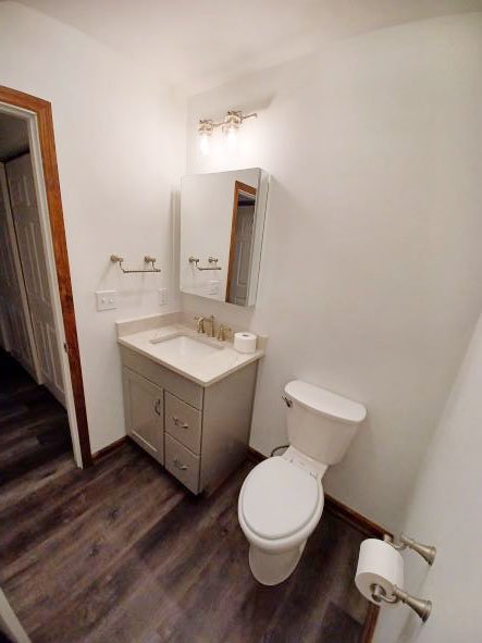 Bathroom remodeled by KBC
Simple clean bathroom. Plank flooring. Vanity with nickel faucets and handles and white square undermount sink. Light fixtures on wall over mirrored medicine cabinet. White toilet on right side of vanity. Toilet paper holder