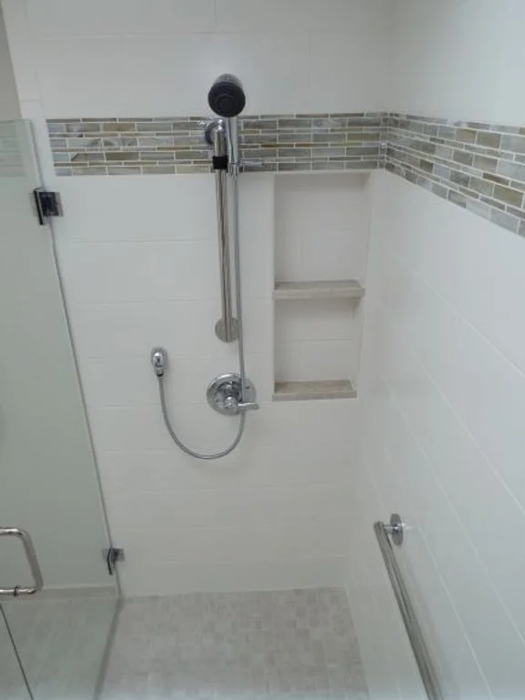 Inside a barrier-free shower with built-in shelves and a hand-held shower sprayer. Glass shower doors are on the left side of the photo.  A grab bar is on the wall on the right side of the photo.
