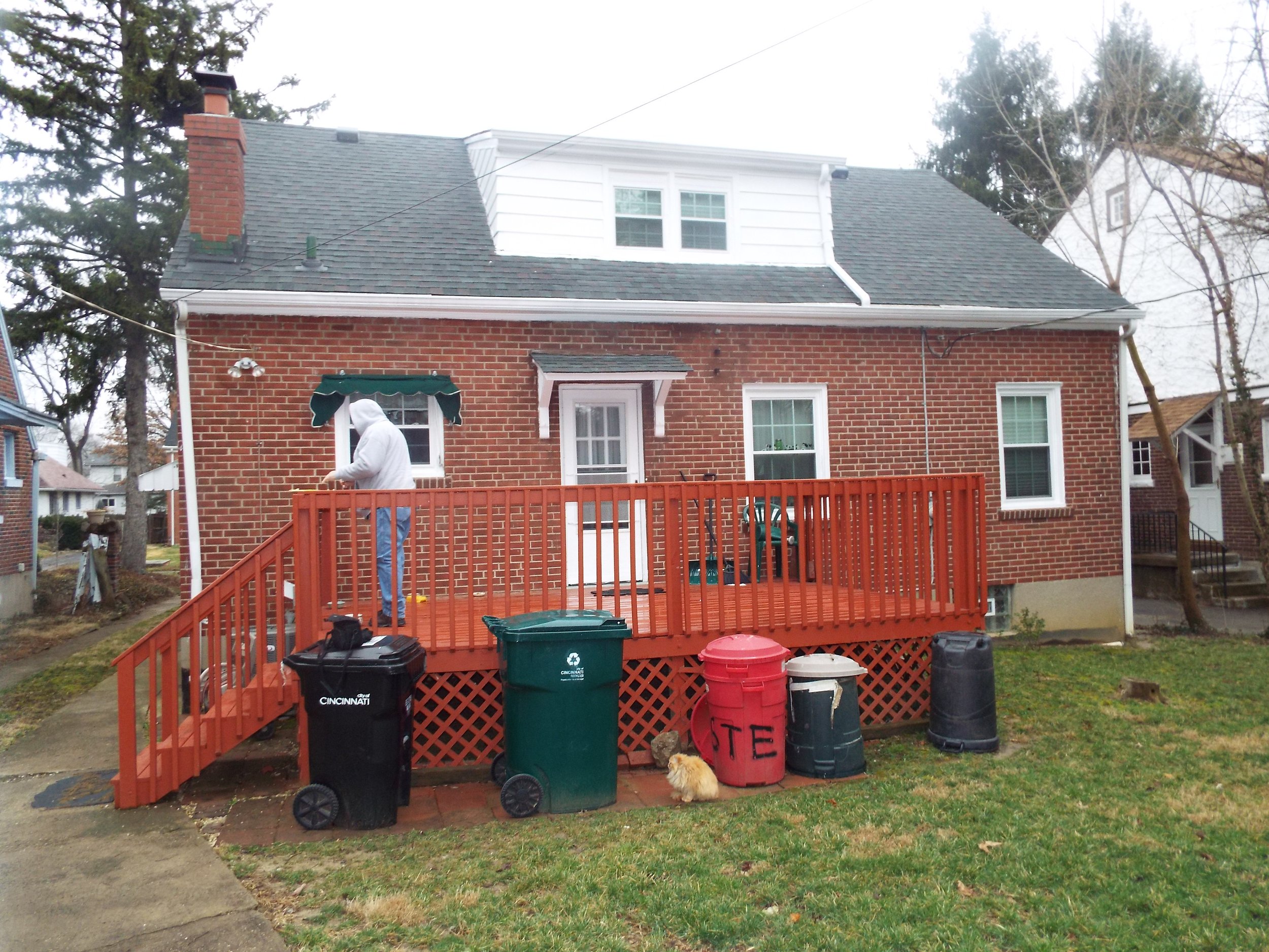 Outdoor view before construction - Woman standing on large deck and garbage cans