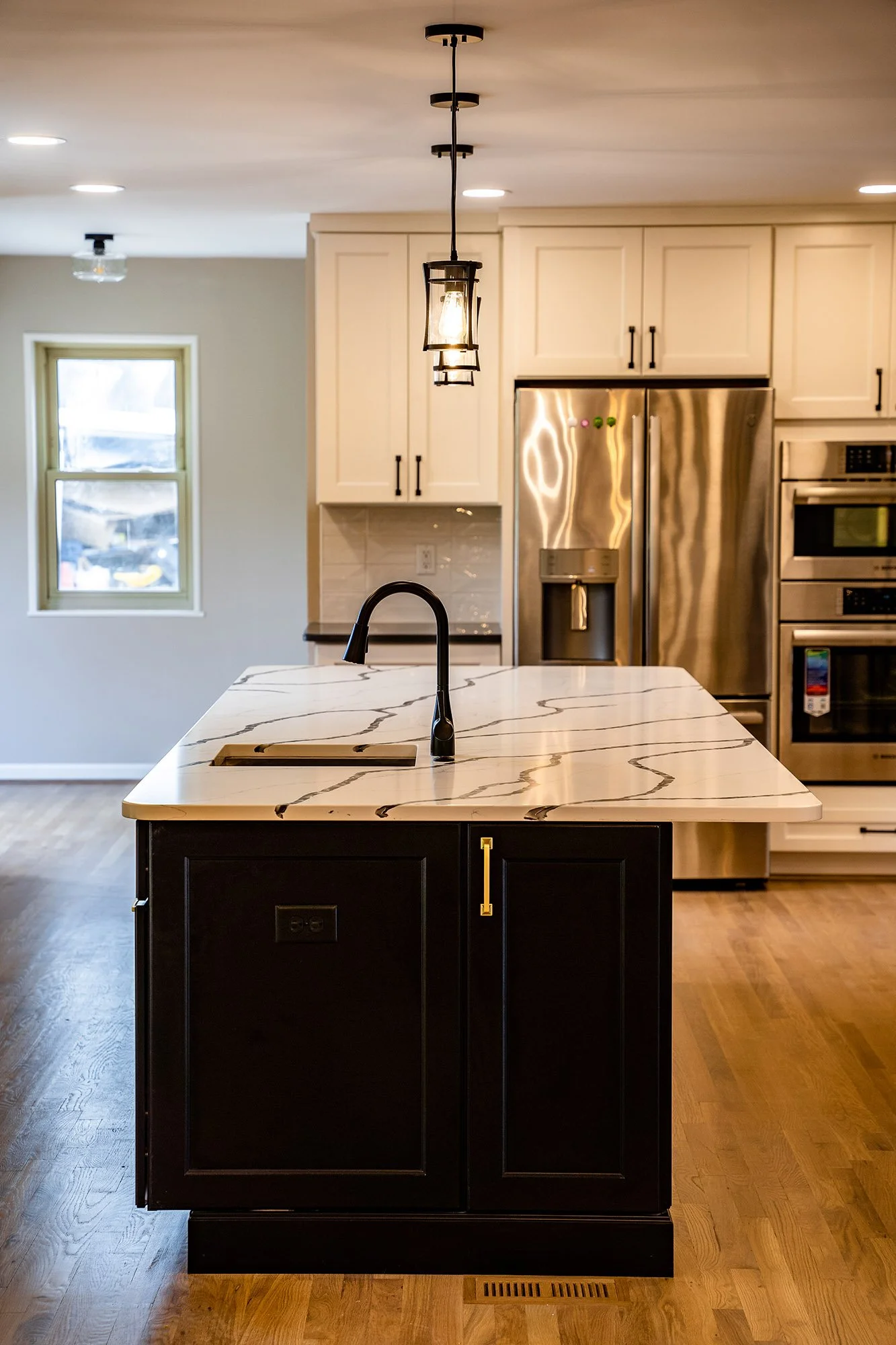 Complete First Floor Remodel by KBC Inc. 
View of kitchen area on left side of photo. LED Can lighting and pendant lighting over a large kitchen island with marble top and prep sink. Stainless steel refrigerator, double oven, and cabinet storage area