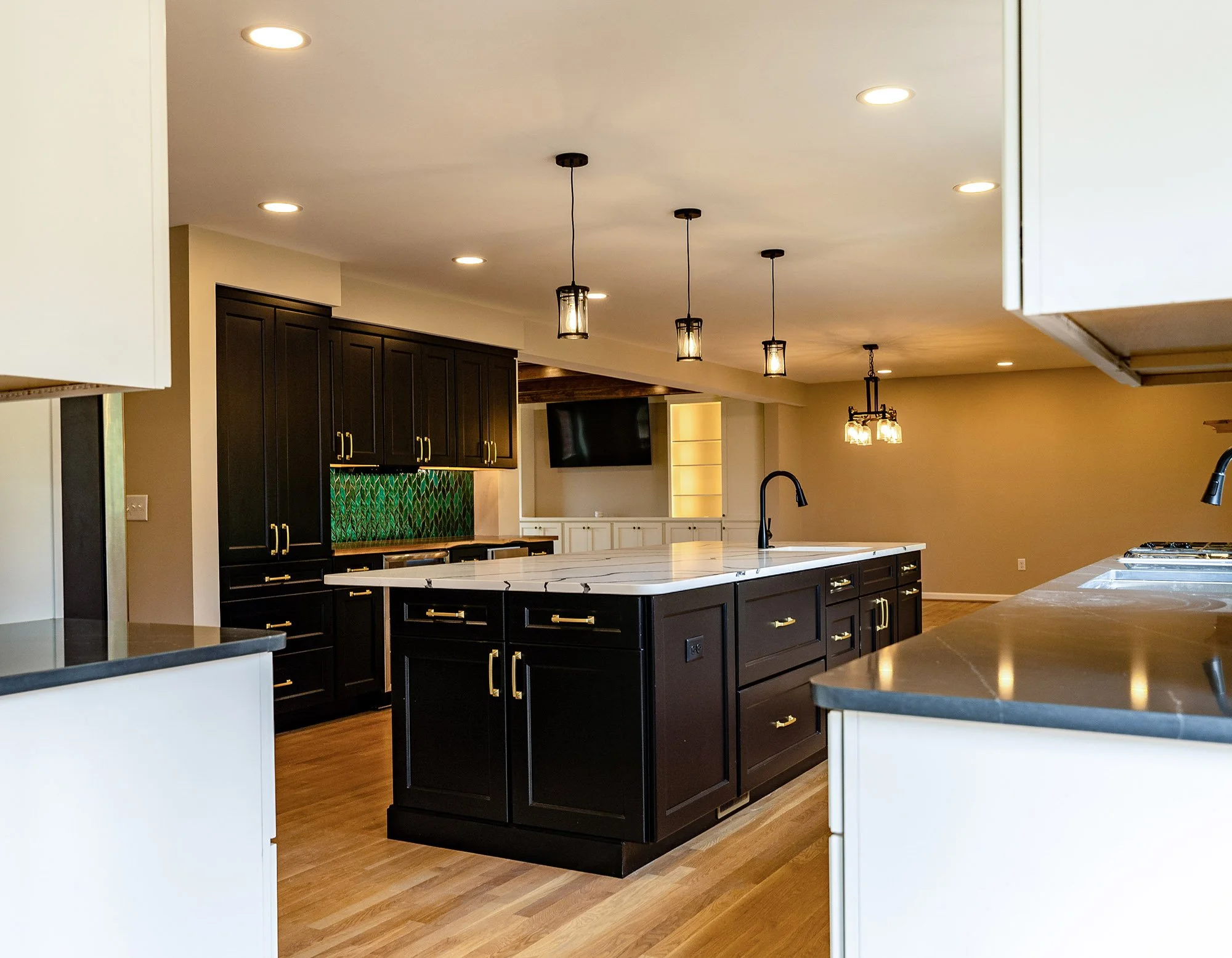 Complete First Floor Remodel by KBC Inc. View of an open concept kitchen, taken from extreme corner angle. Woodgrain counter with tiled backsplash and dark upper and lower cabinets with wine chiller and stainless steel dishwasher. In center, large ki