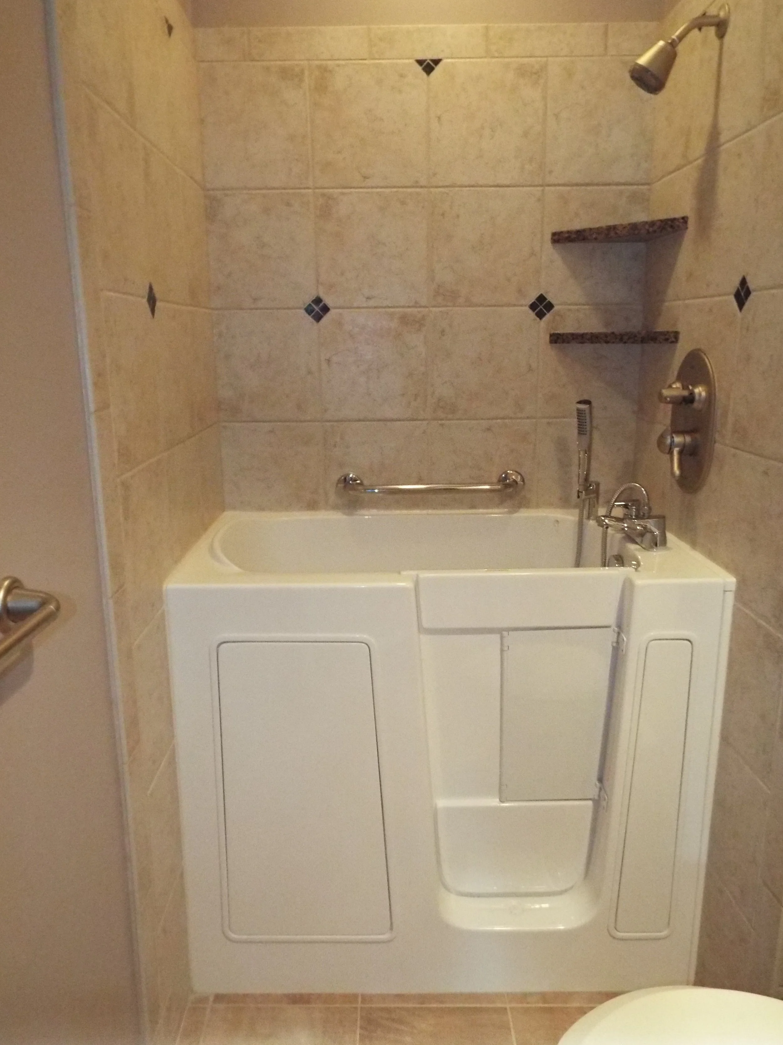 White tub and shower area in a remodeled bathroom. Cararra marble dark diamond pattern on shower walls. Cararra marble on floors. White walk-in tub. Brushed metal fixtures in shower.