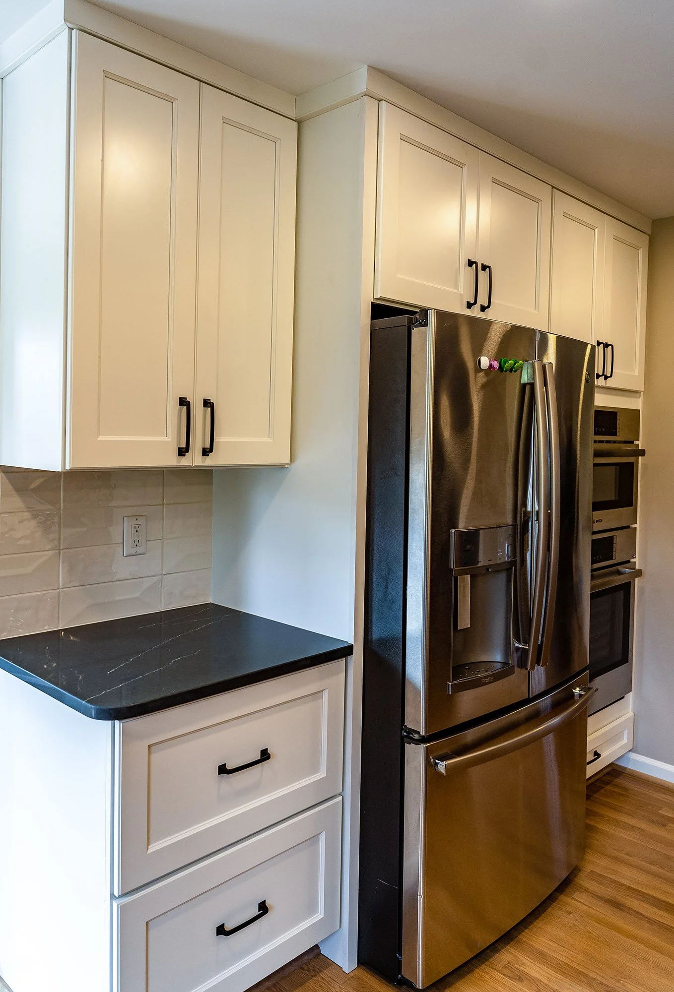 Complete First Floor Remodel by KBC Inc. 
Close up view of kitchen area. Small counter for prep, double ovens and stainless steel refrigerator with cabinet storage. Wooden plank flooring.
