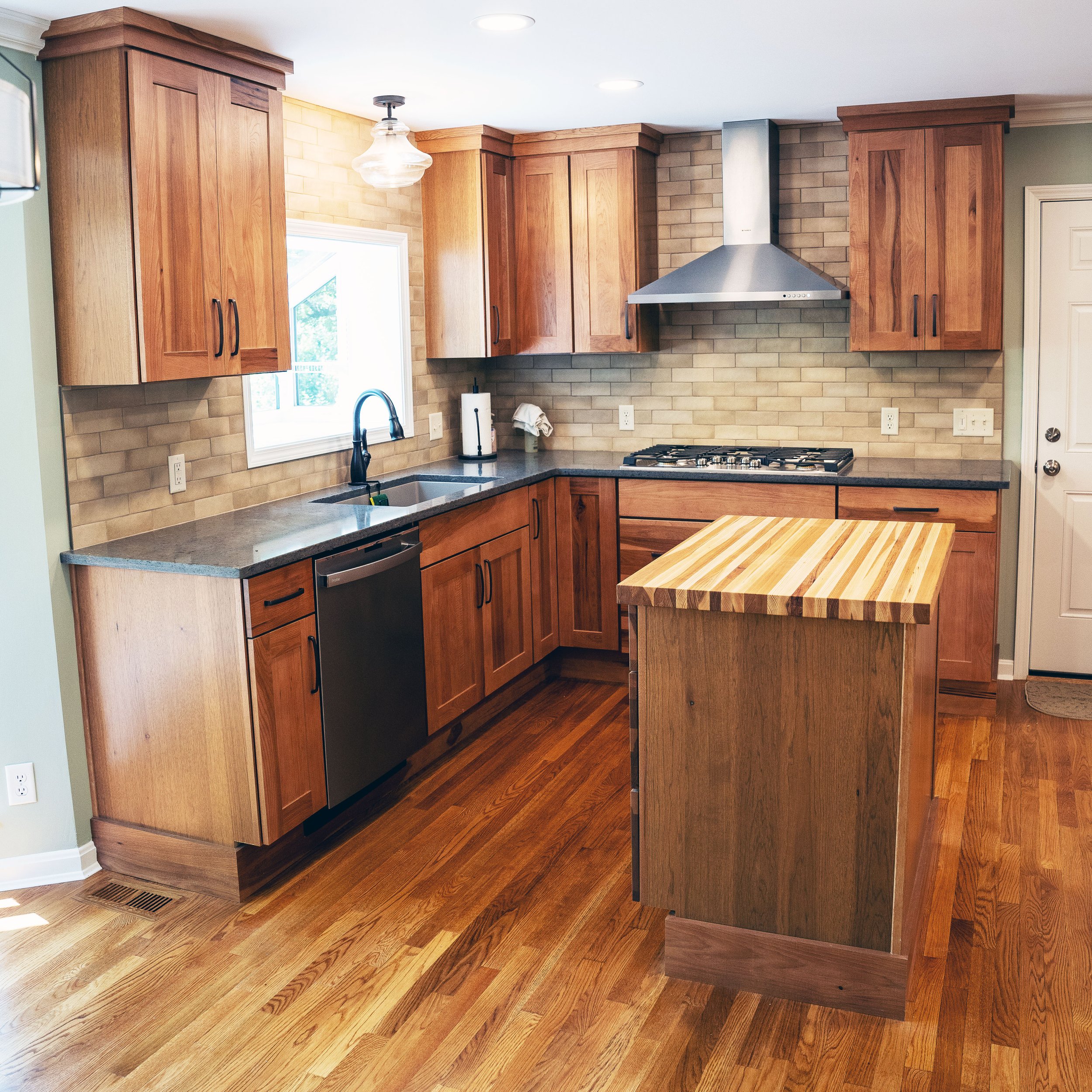 KBC Construction - Whole House Remodel in Lakeside Park, KY. Kitchen with brick backsplash and darker wood cabinets. A butcher block island on darker wood  cabinets.A stainless steel range hood is over the stove on the back wall. The faucet and sink 