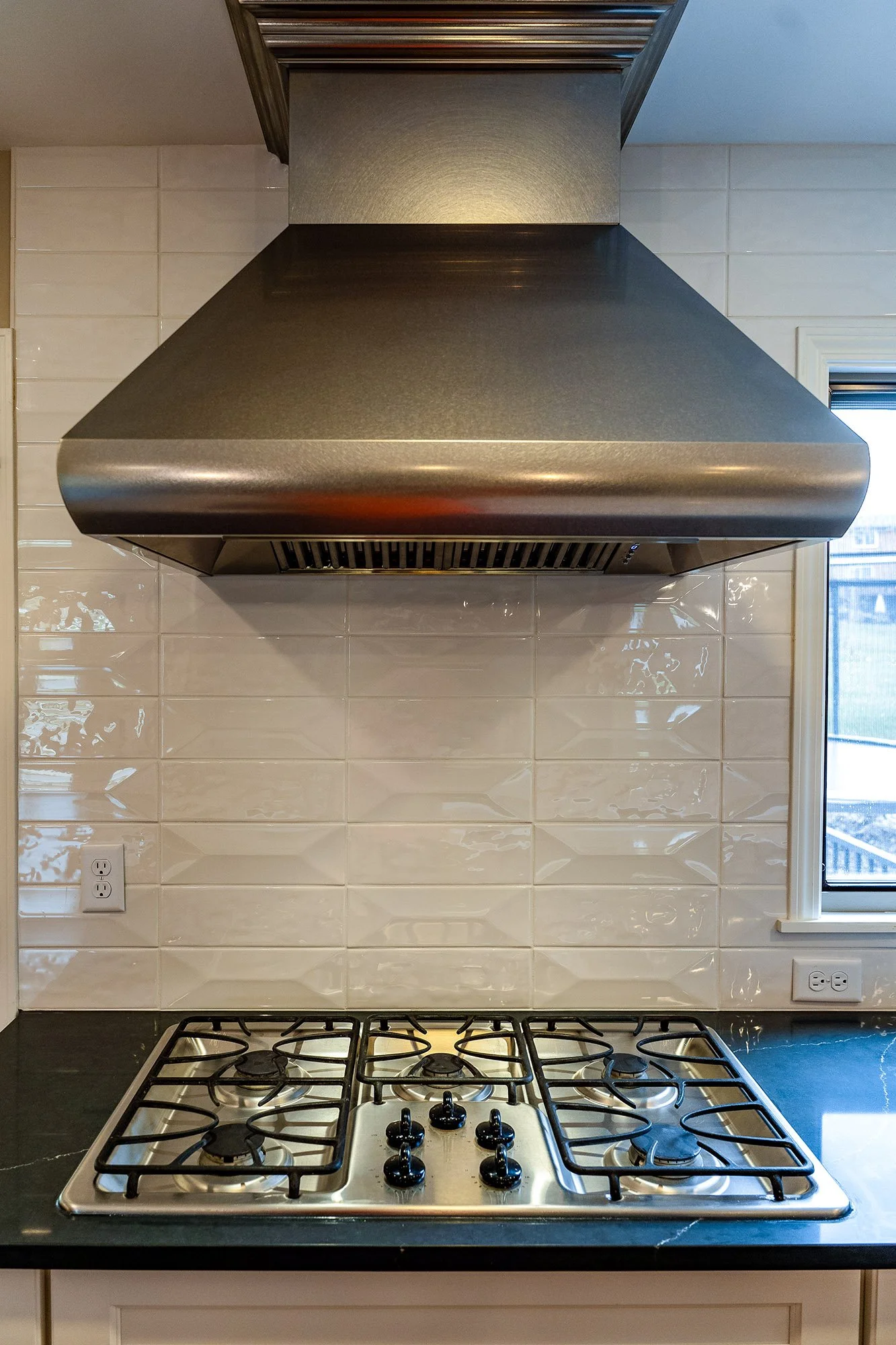 Complete First Floor Remodel by KBC Inc. Closeup view of exhaust hood over gas stove burners mounted in dark countertop. White subway tile backsplash. 