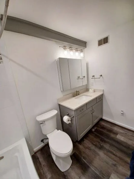 Bathroom remodeled by KBC
Simple clean bathroom. Plank flooring. Large vanity with nickel faucets and handles and white square undermount sink. Light fixtures on wall over three-sectioned mirrored medicine cabinet. Toilet paper holder mounted on vani