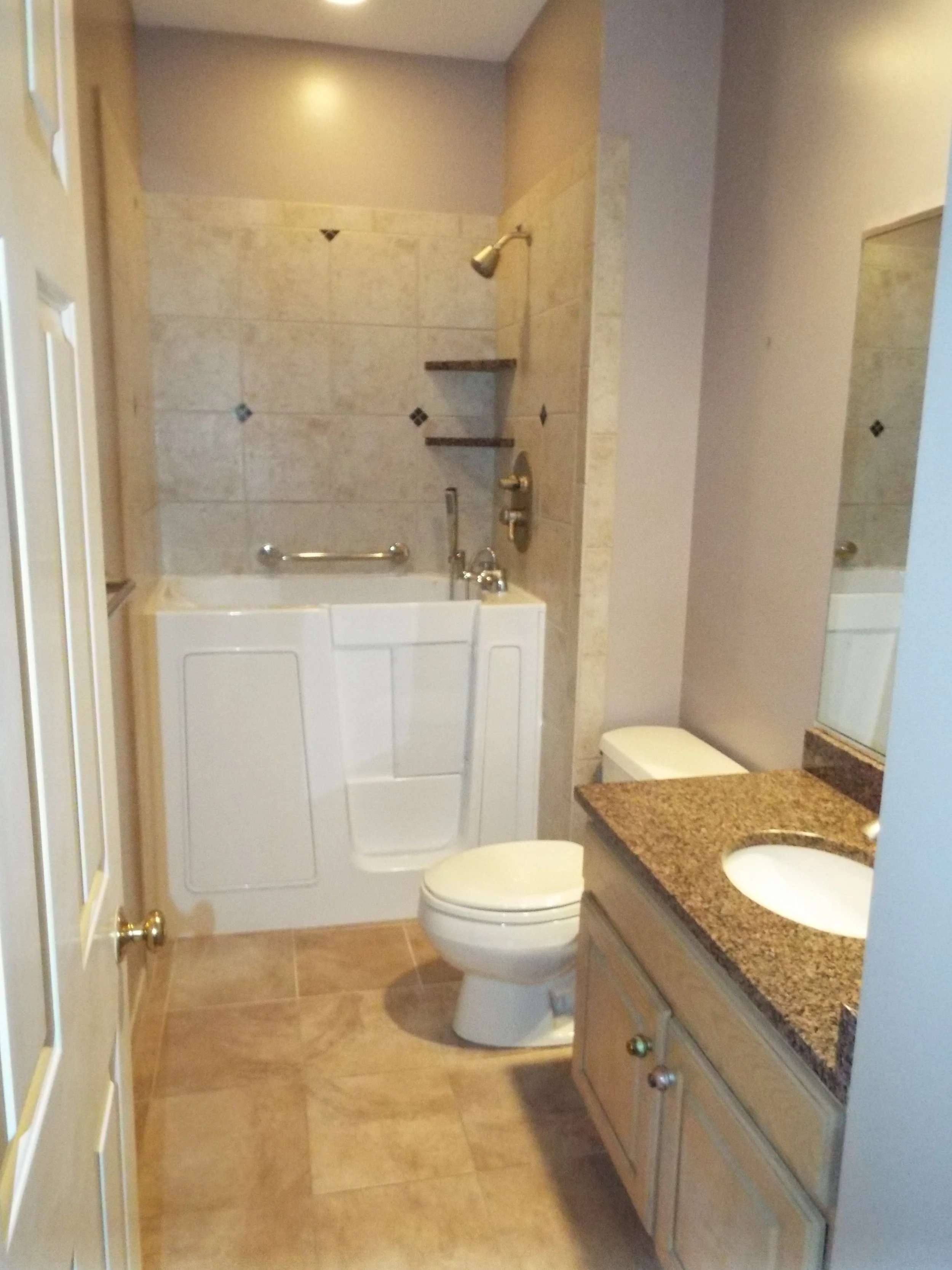 Remodeled bathroom. Cararra marble dark diamond pattern on shower walls. Cararra marble on floors. White walk-in tub. White toilet. White vanity with dark marble sinktop and white undermounted sink. Brushed metal fixtures in shower and sink. A large 