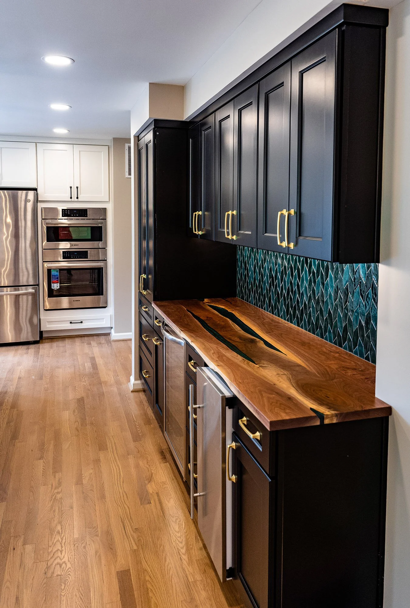 Complete First Floor Remodel by KBC Inc. Cabinet storage with a large woodgrain counter. Tiled backsplash on right side of photo. LED lighting. Oven and other kitchen appliances visible on left side of photo. 