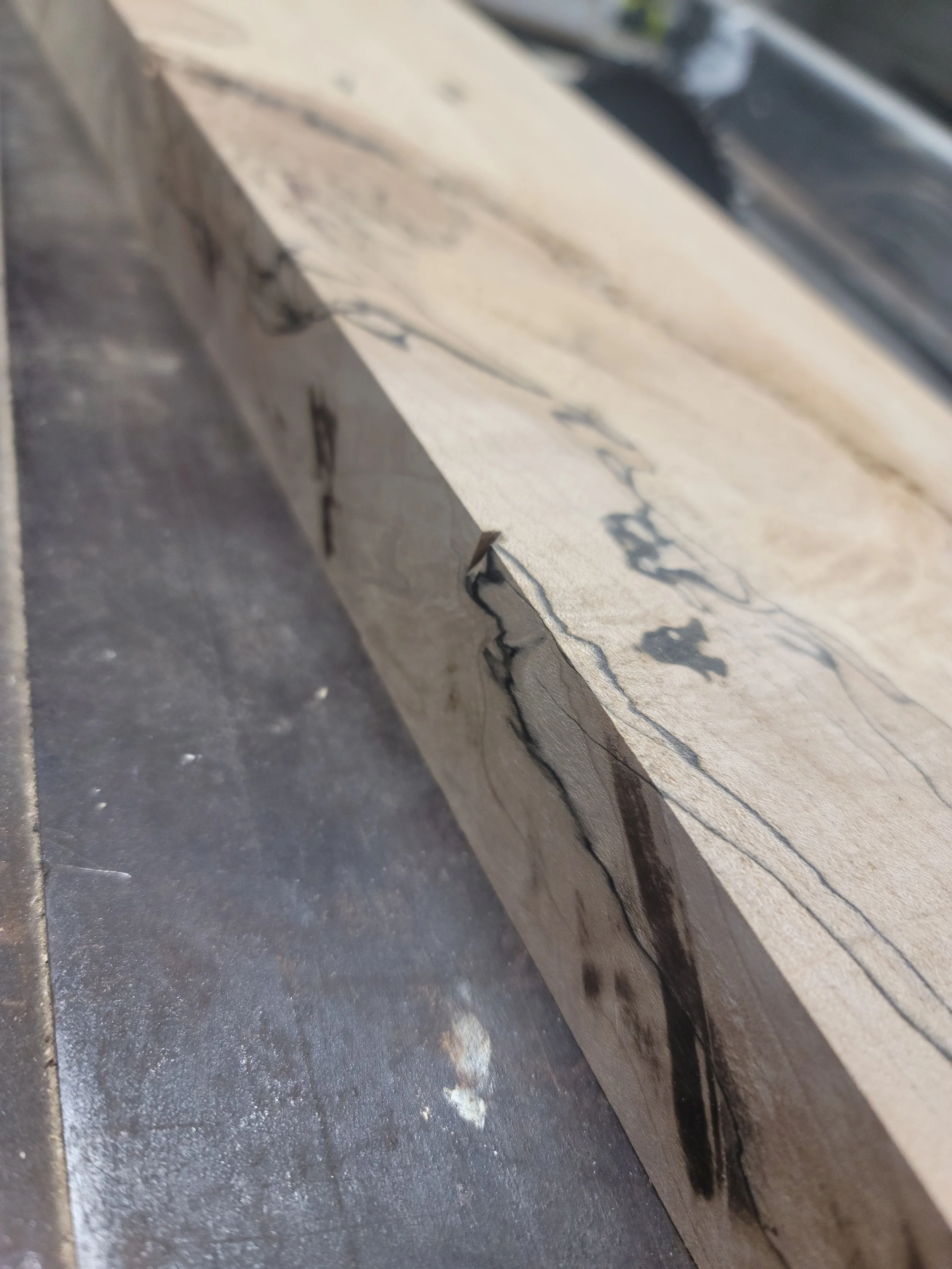 A close-up of a piece of wood with dark veins or streaks, resting on a dark surface.