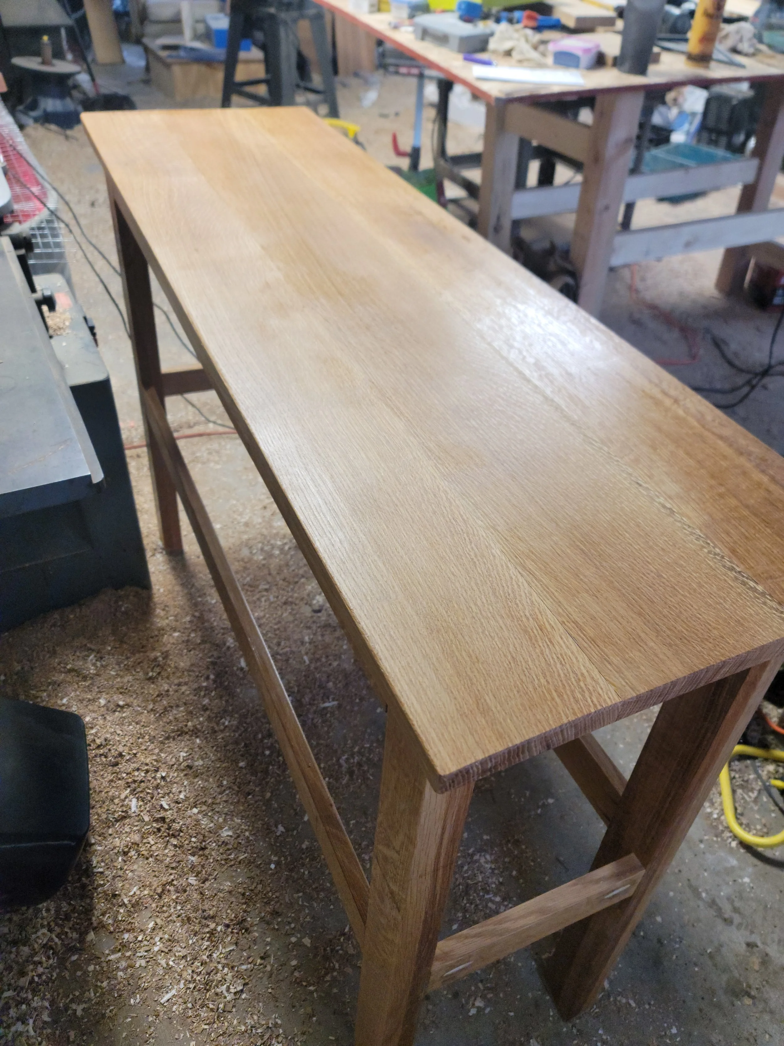 Wooden workbench in a woodworking shop with tools and supplies in the background.
