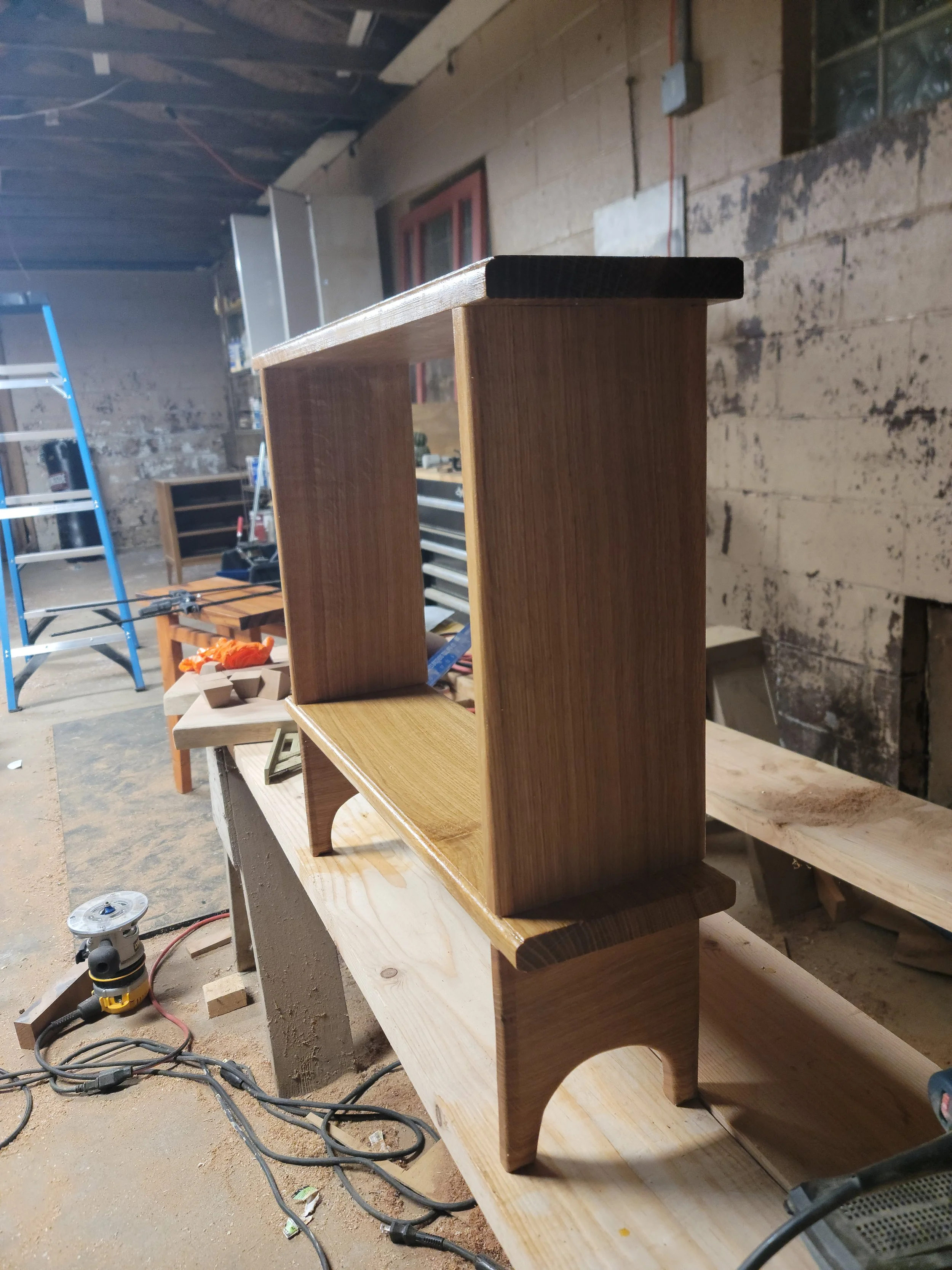 A small wooden shelf or stand with curved legs on a workbench in a carpentry workshop.