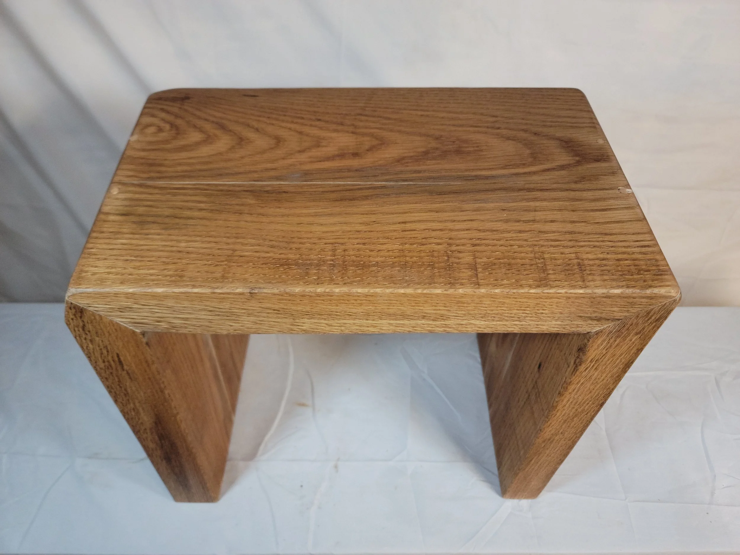 A small wooden stool with a rectangular top and curved legs, made of light-colored wood with visible grain patterns.