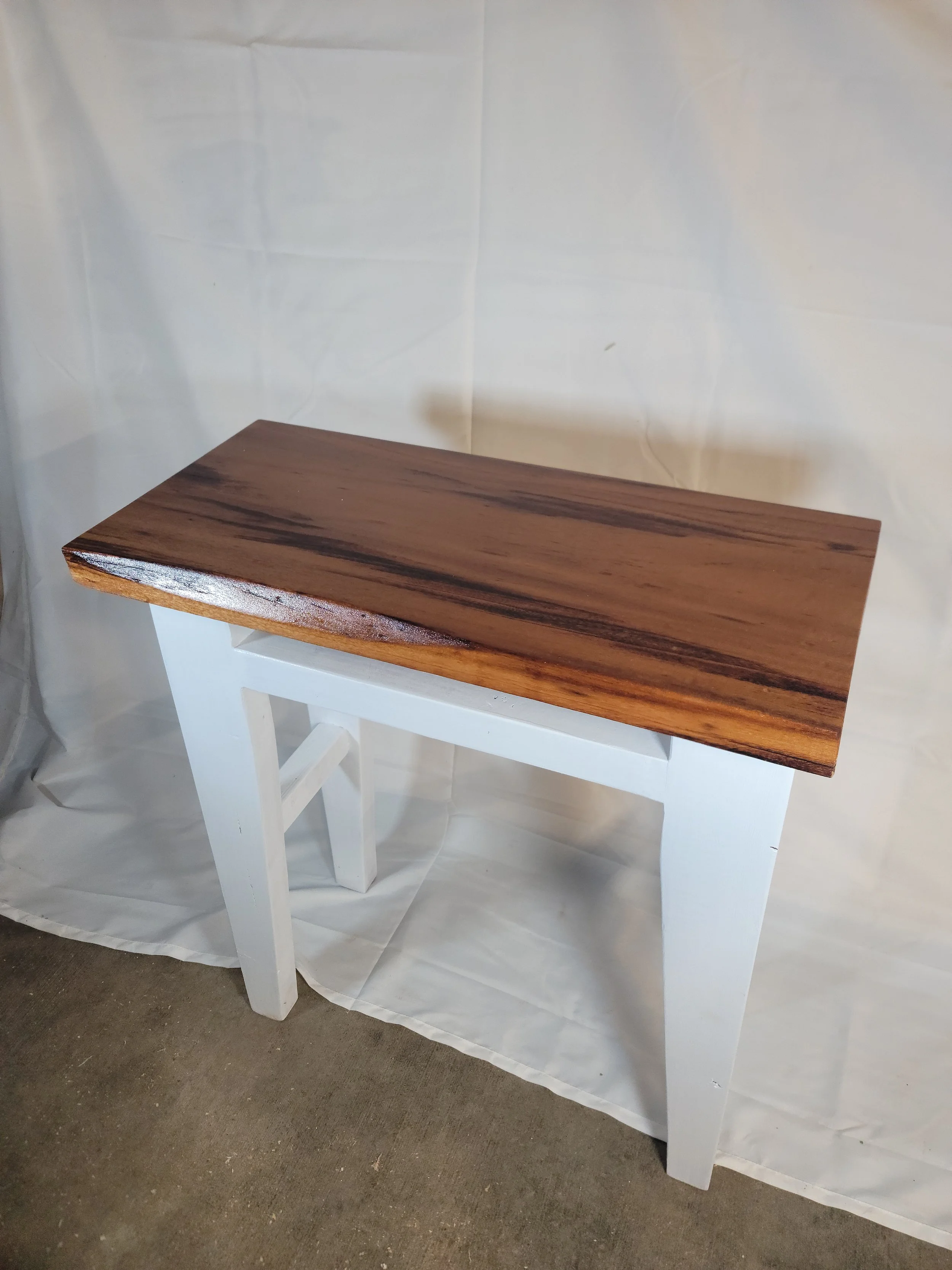 A small wooden table with a dark wood top and white legs against a plain background.