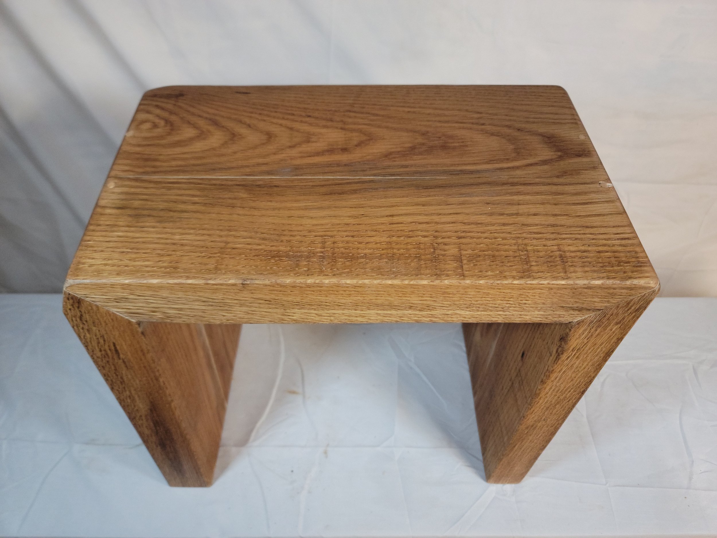 A wooden stool with a rectangular top and two angled legs.