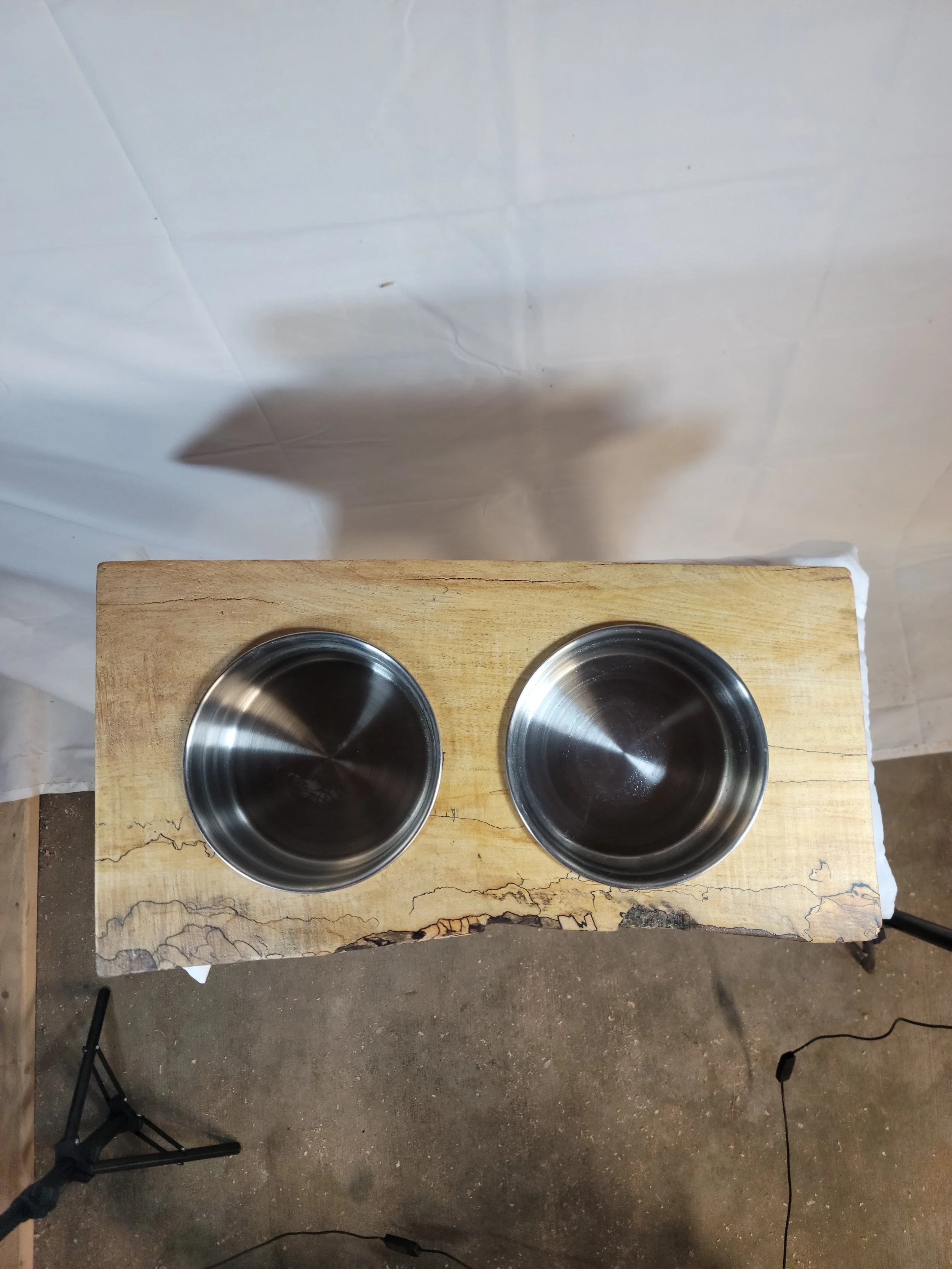 Two metal pet bowls placed on a wooden surface, with a white background and a shadow cast on the backdrop.