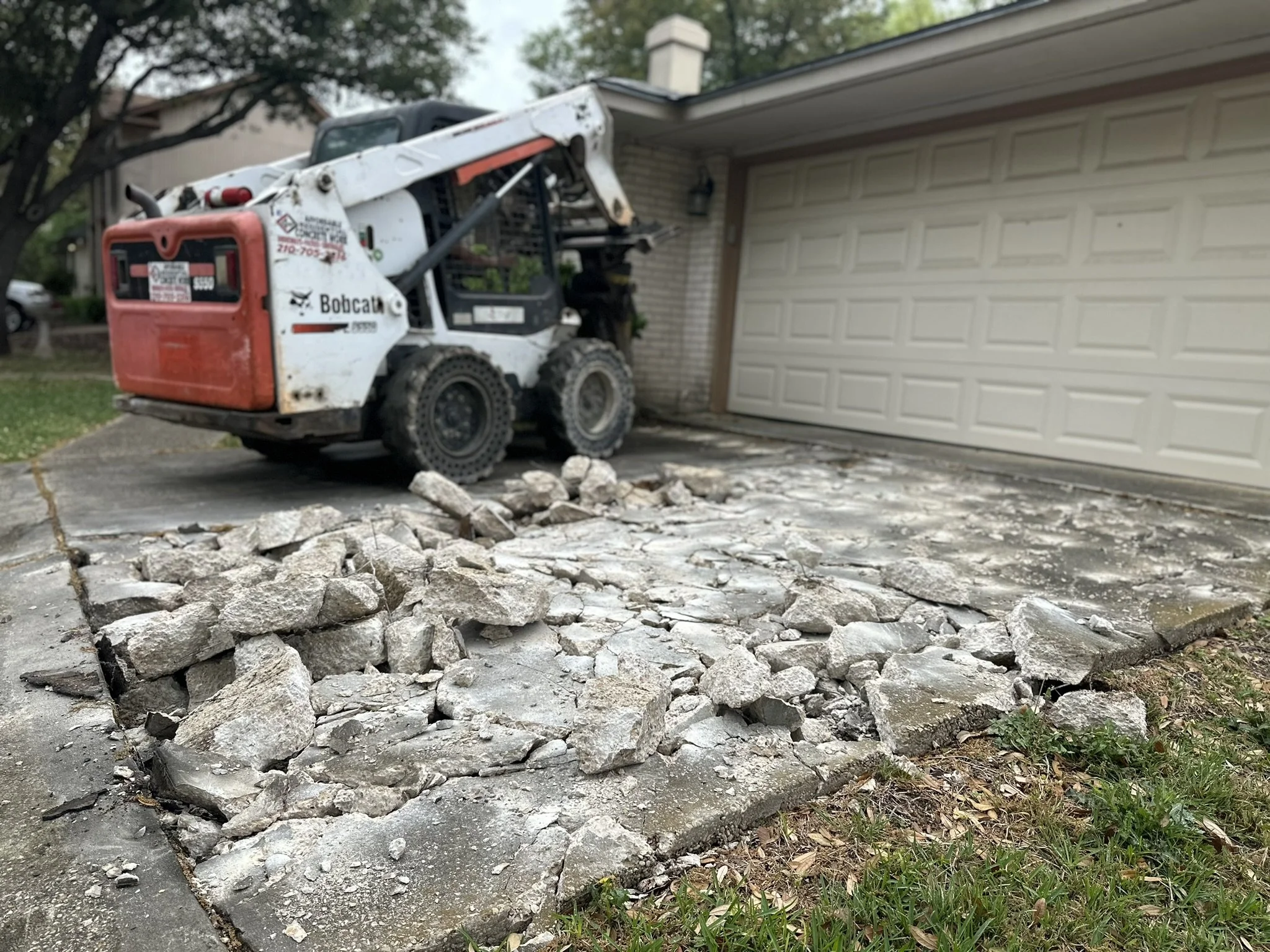 Residential concrete driveway demolition in San Antonio, TX. Affordable Concrete & Construction removing the existing damaged concrete with professional equipment before preparing the area for a new reinforced concrete driveway.