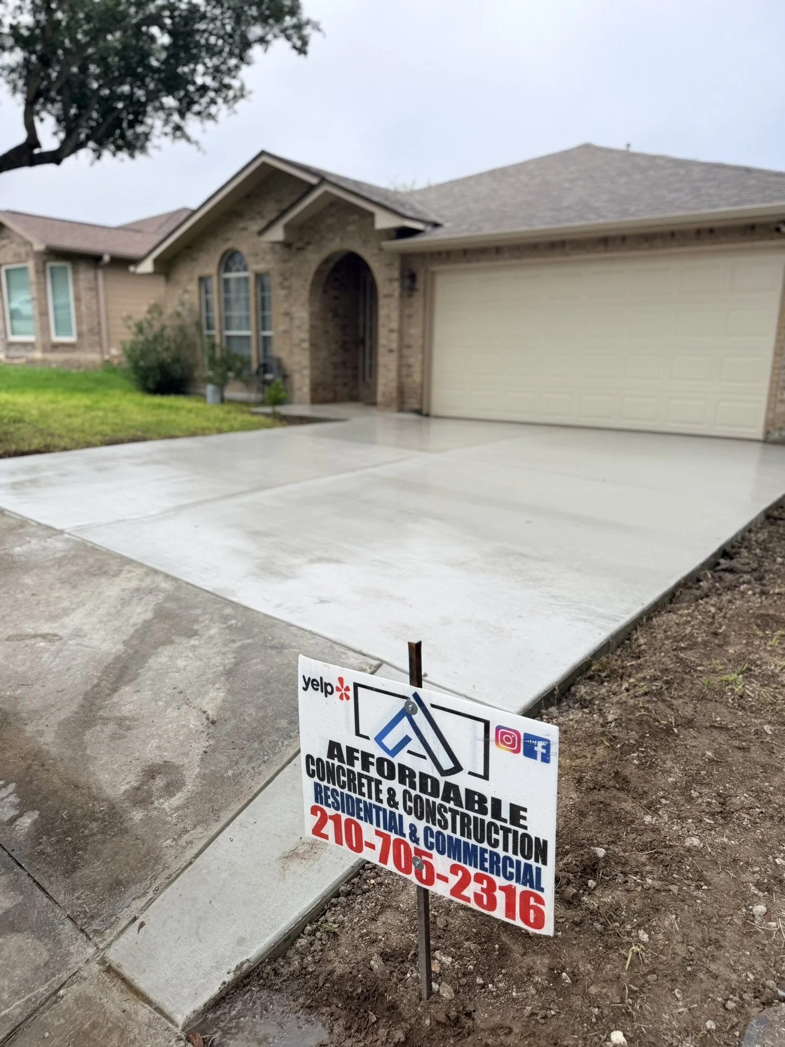 New concrete driveway and sidewalk in front of a house under construction. There is a sign with contact information for the construction company.
