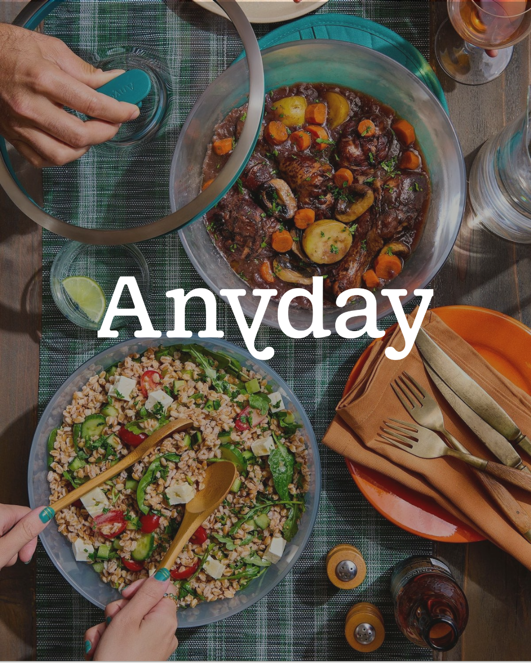 A table with seasoned beef stew, a mixed grain salad with vegetables and feta, and drinks, set with cutlery, napkins, and condiments for a family dinner.
