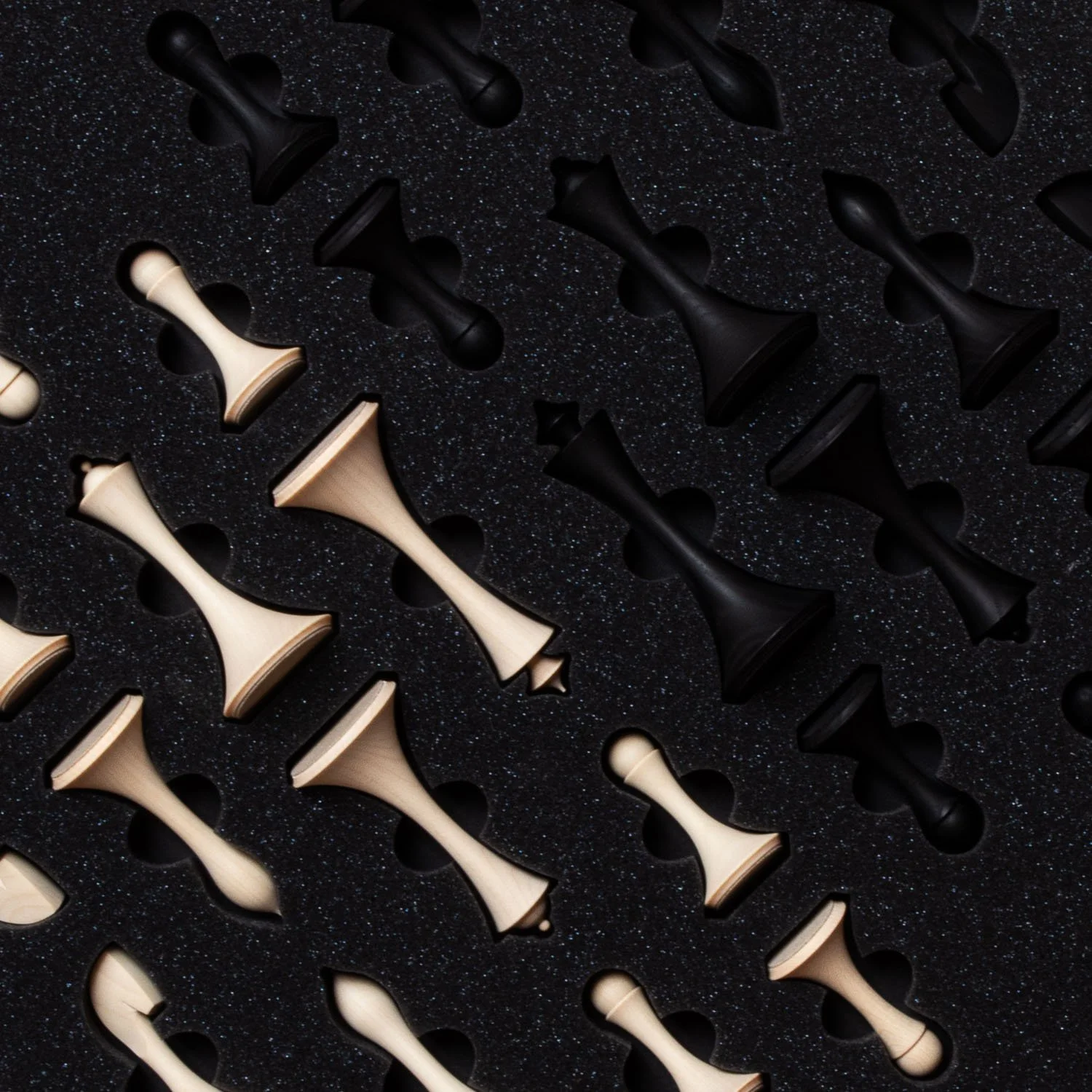 Close-up of a textured black surface with evenly spaced light and dark chess pieces.