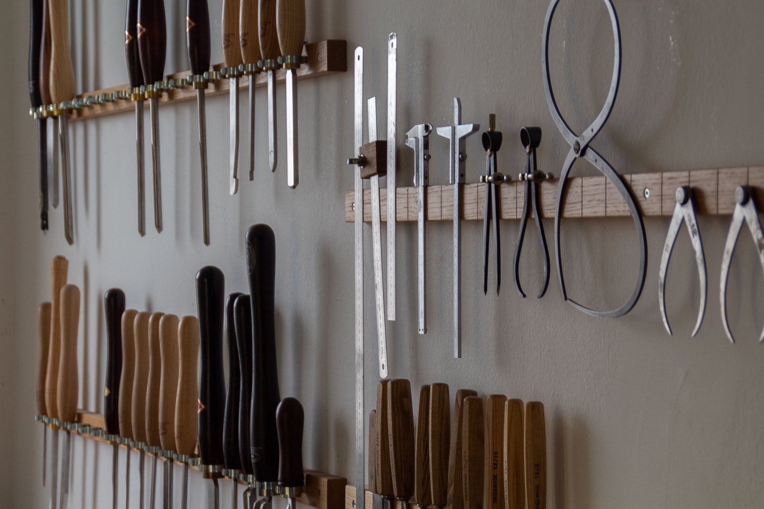 Wall with woodworking tools including chisels, clamps, and saws organized on hooks and a wooden rack.