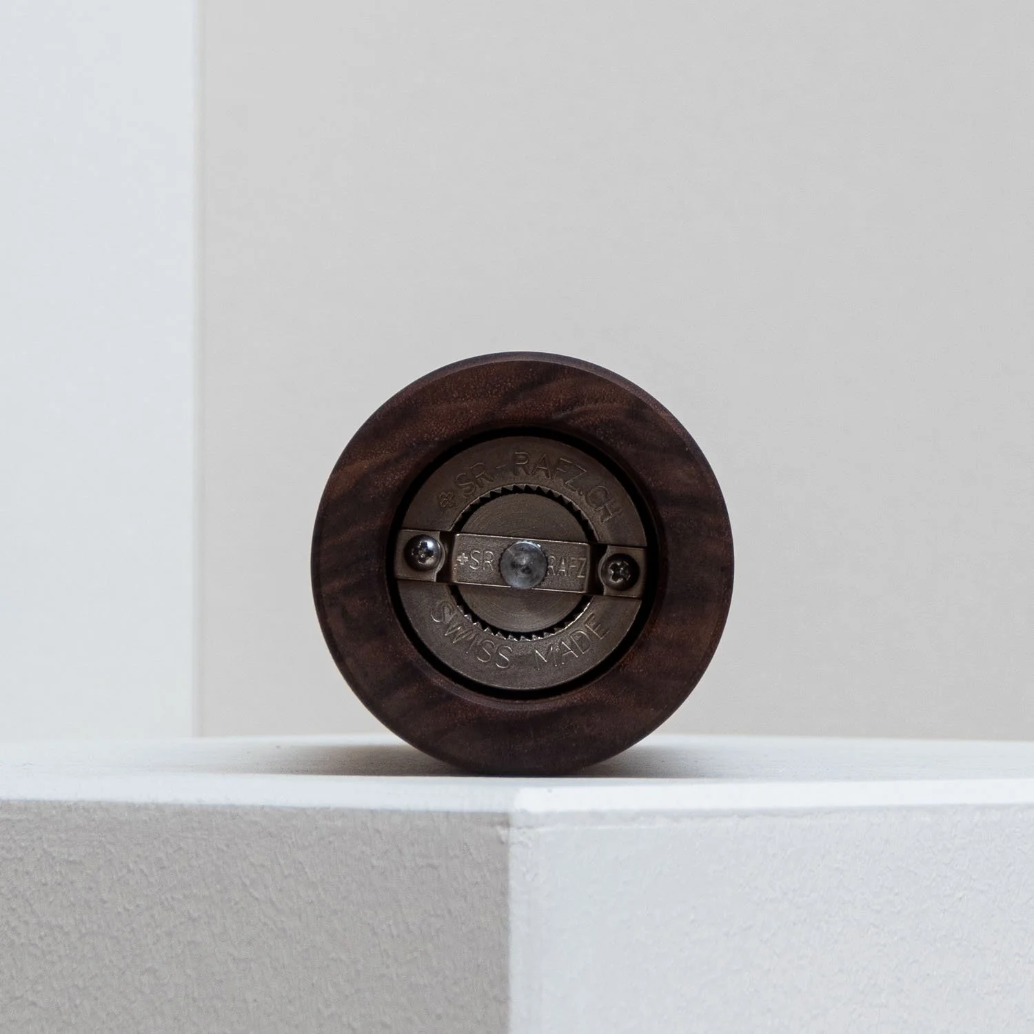 Close-up of a circular mechanical device with a wooden frame, mounted on a white surface against a gray background.