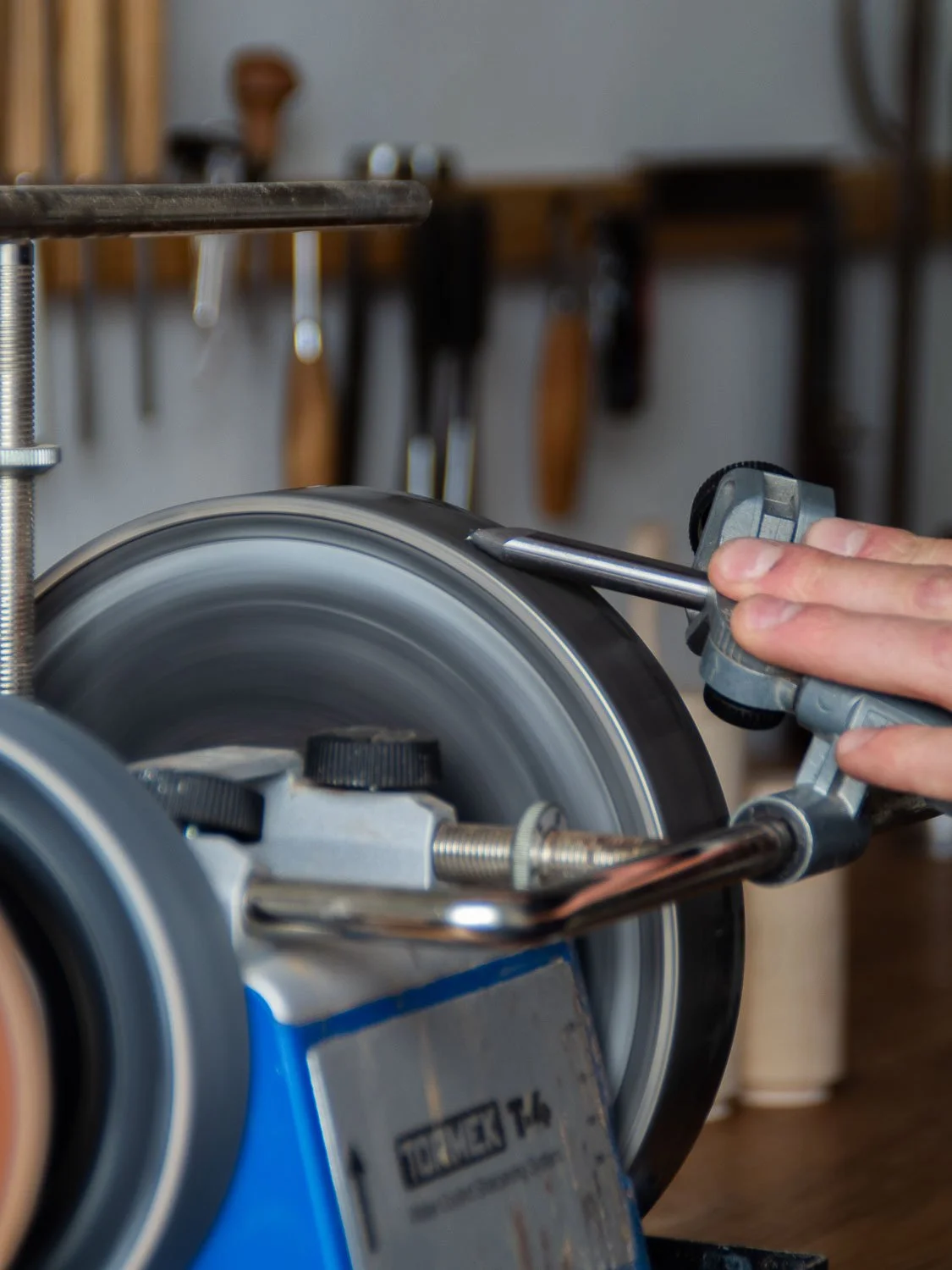A person using a blade sharpener on a circular saw blade, with woodworking tools hanging on the wall in the background.