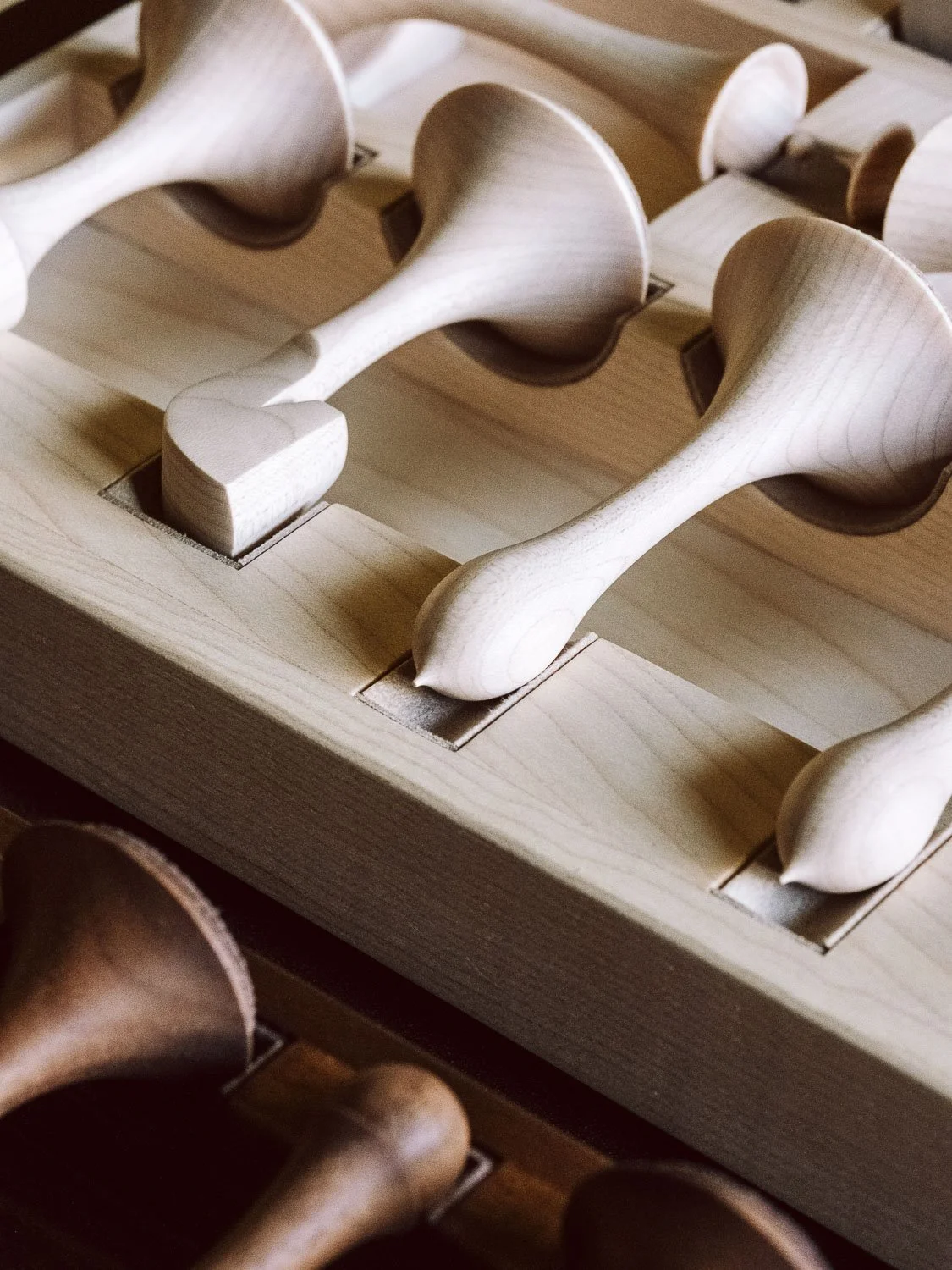 Close-up of wooden chess pieces on a wooden chessboard, showing the tops of some king and queen pieces.