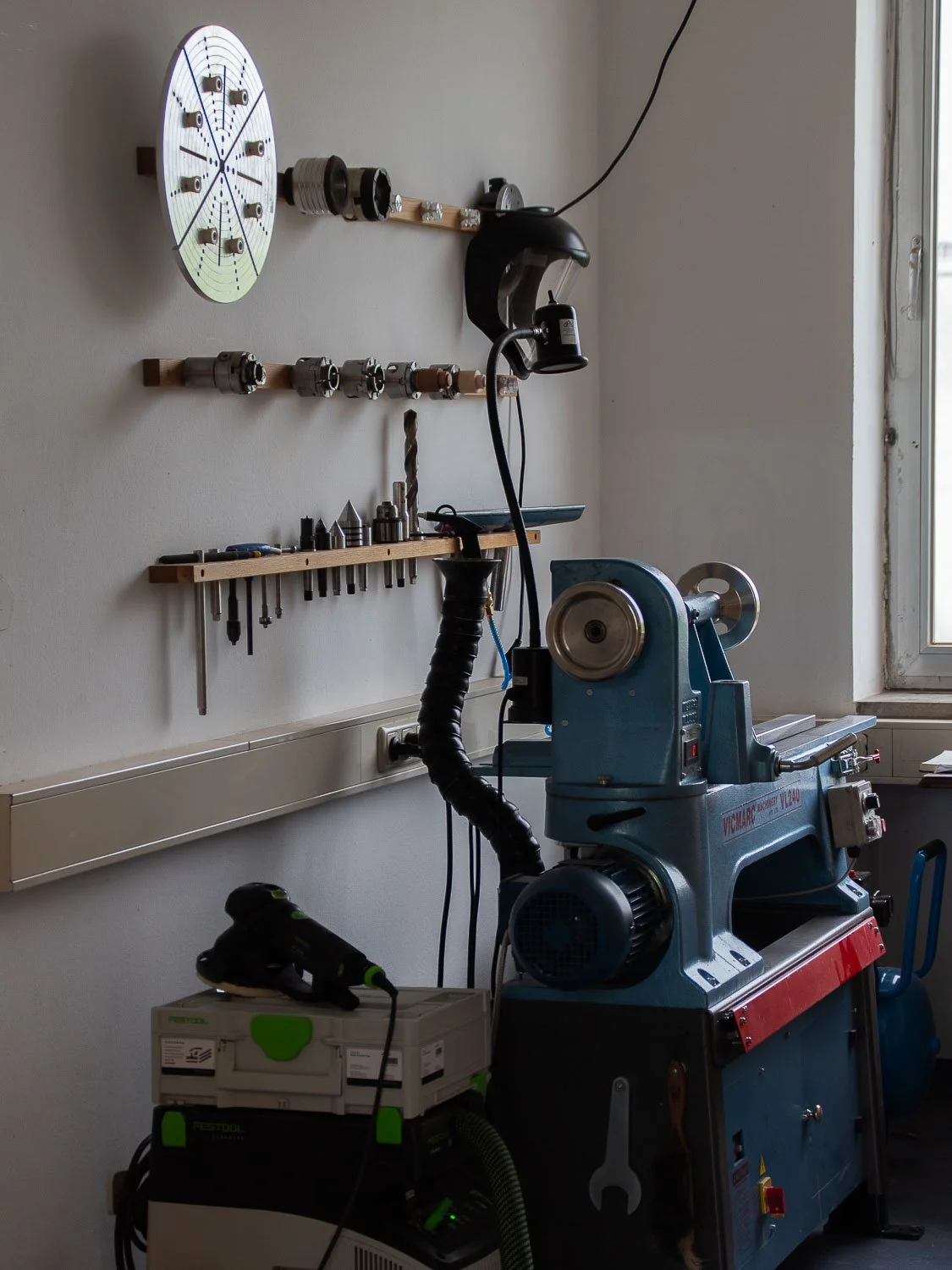 Workshop with a lathe machine, tool rack, and wall-mounted organizing system for small parts, near a window.
