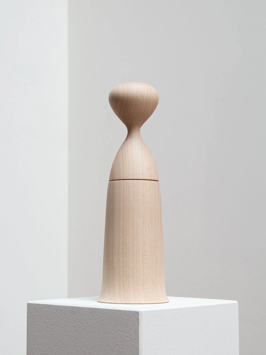 A wooden candy dispenser with a rounded top, displayed on a white pedestal in a minimalist setting.