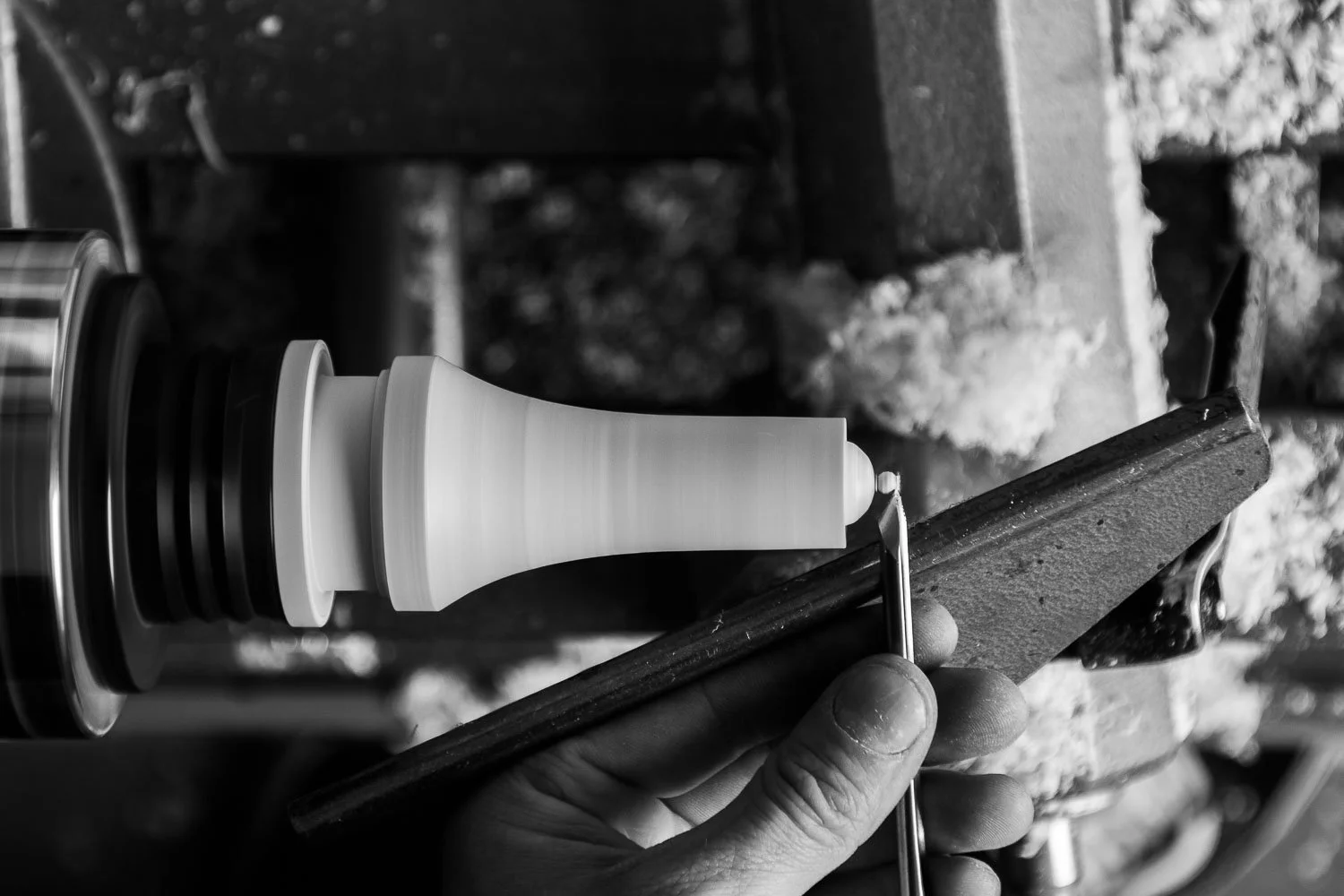 A person holding a chisel and carving a wooden chess pawn on a workbench.